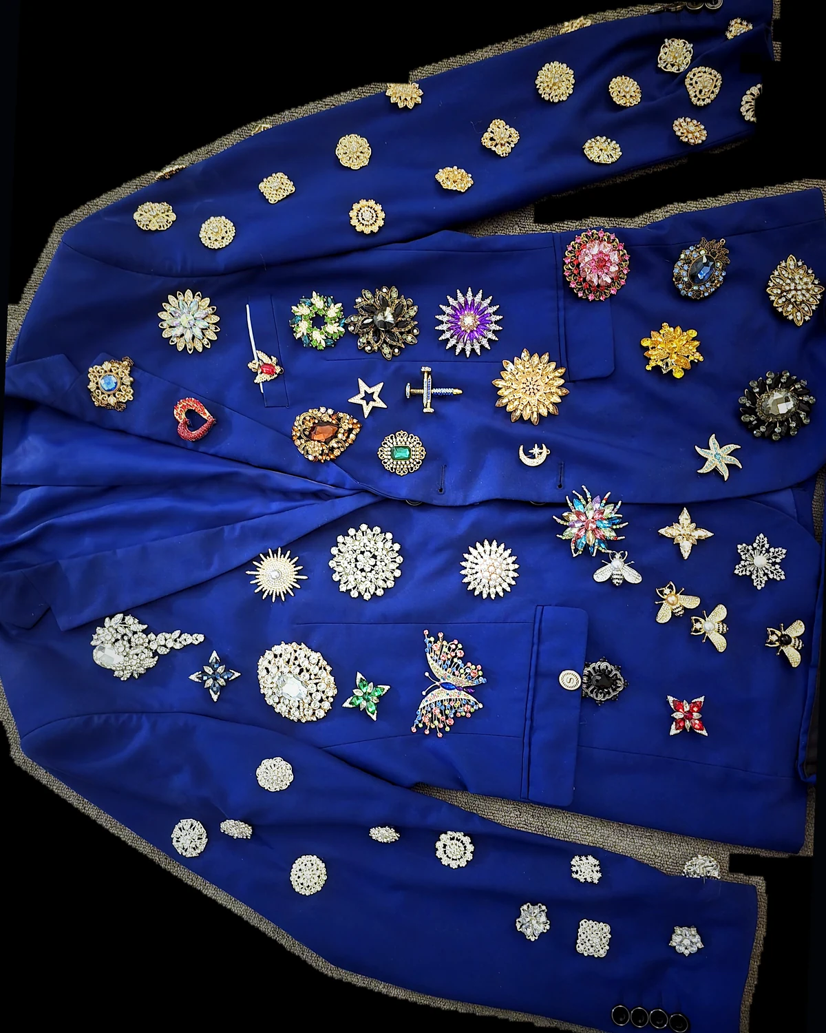 Top-down diagonal view of the Wonder Suit jacket with every original brooch preserved against a dark field.