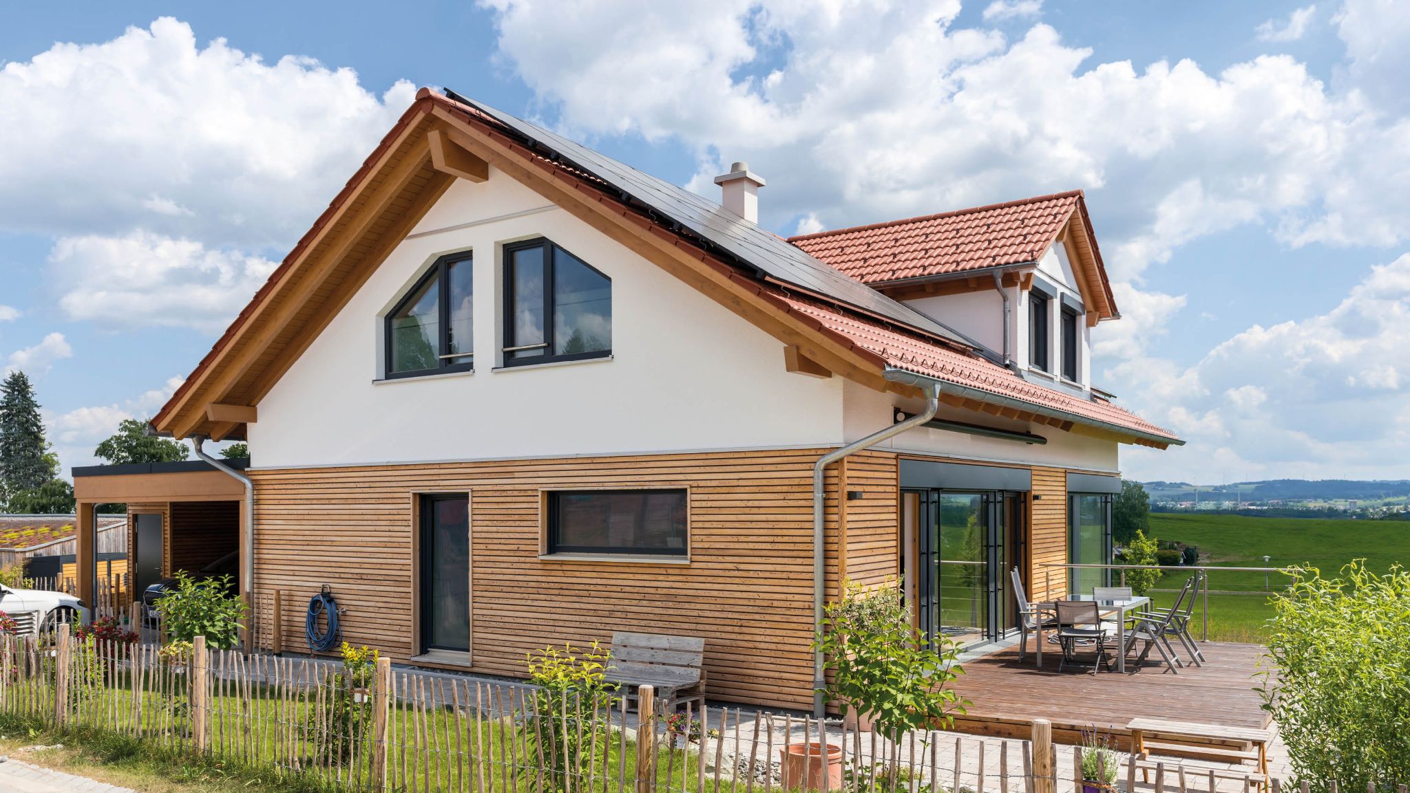 Freistehendes Einfamilienhaus mit Holzfassade, Dachterrasse und Solaranlage auf dem roten Ziegeldach.