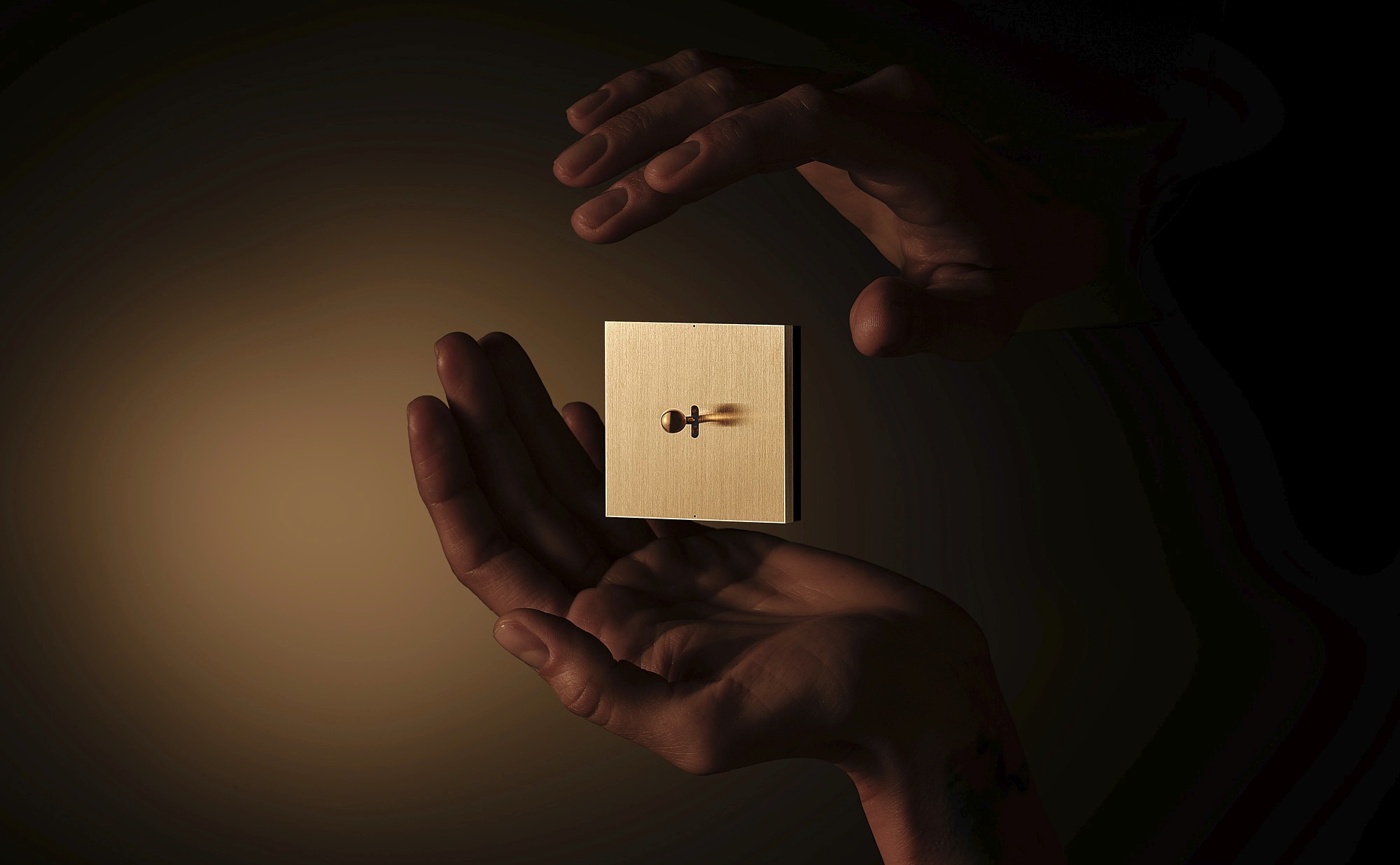 Hands gently hold a small, illuminated box against a dark background, creating a warm, focused glow.