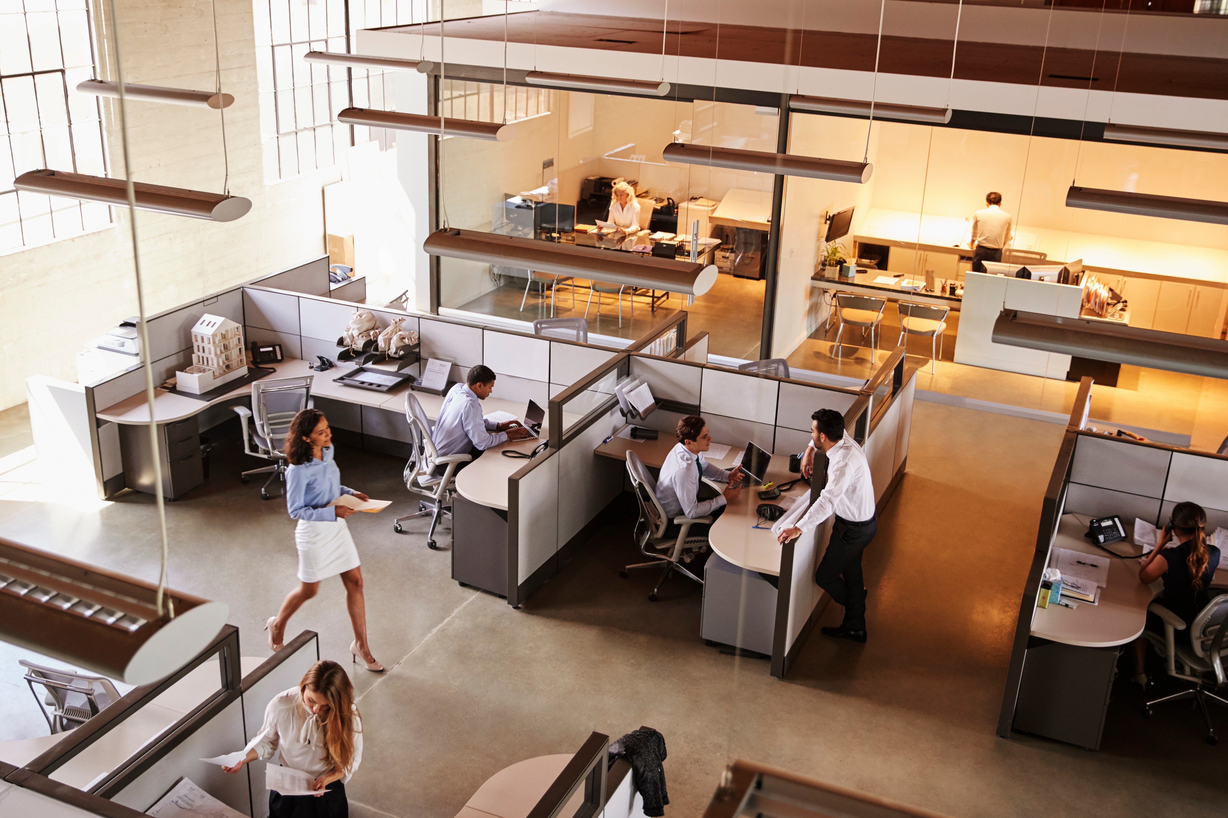 An overhead view of a modern office space with several workstations, showing employees engaged in various tasks. 