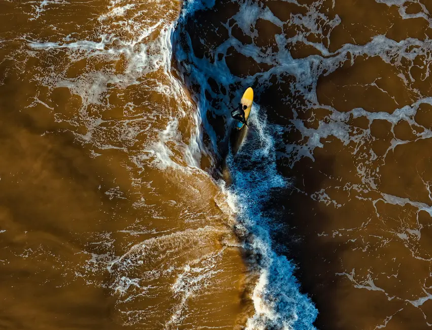 Surfer paddling on a yellow surfboard in brown ocean waves