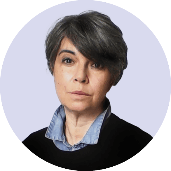 Portrait of a serious looking woman with short dark hair in a dark top, pale background.