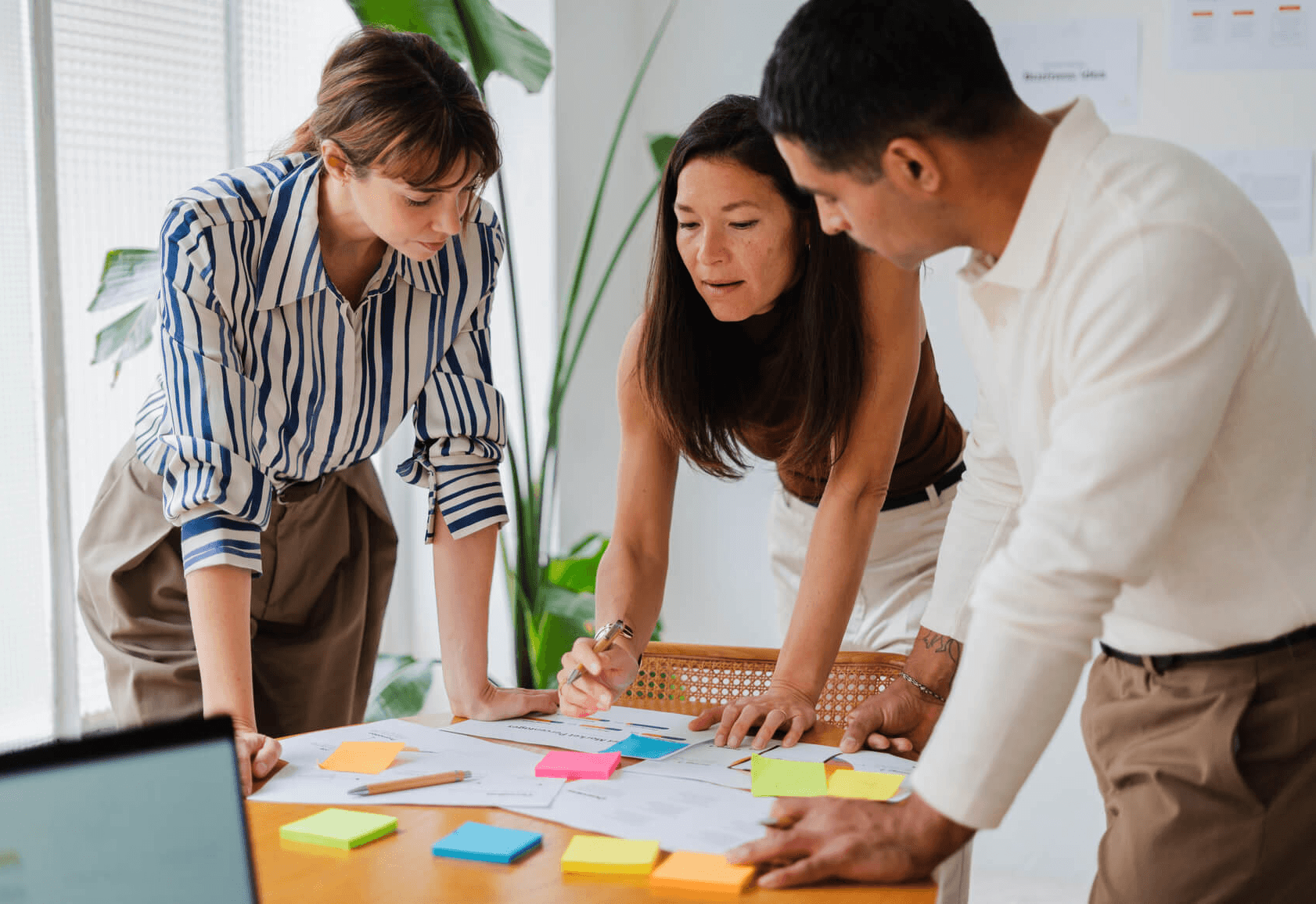 Three team members collaborating over project documents and colorful sticky notes in an office.