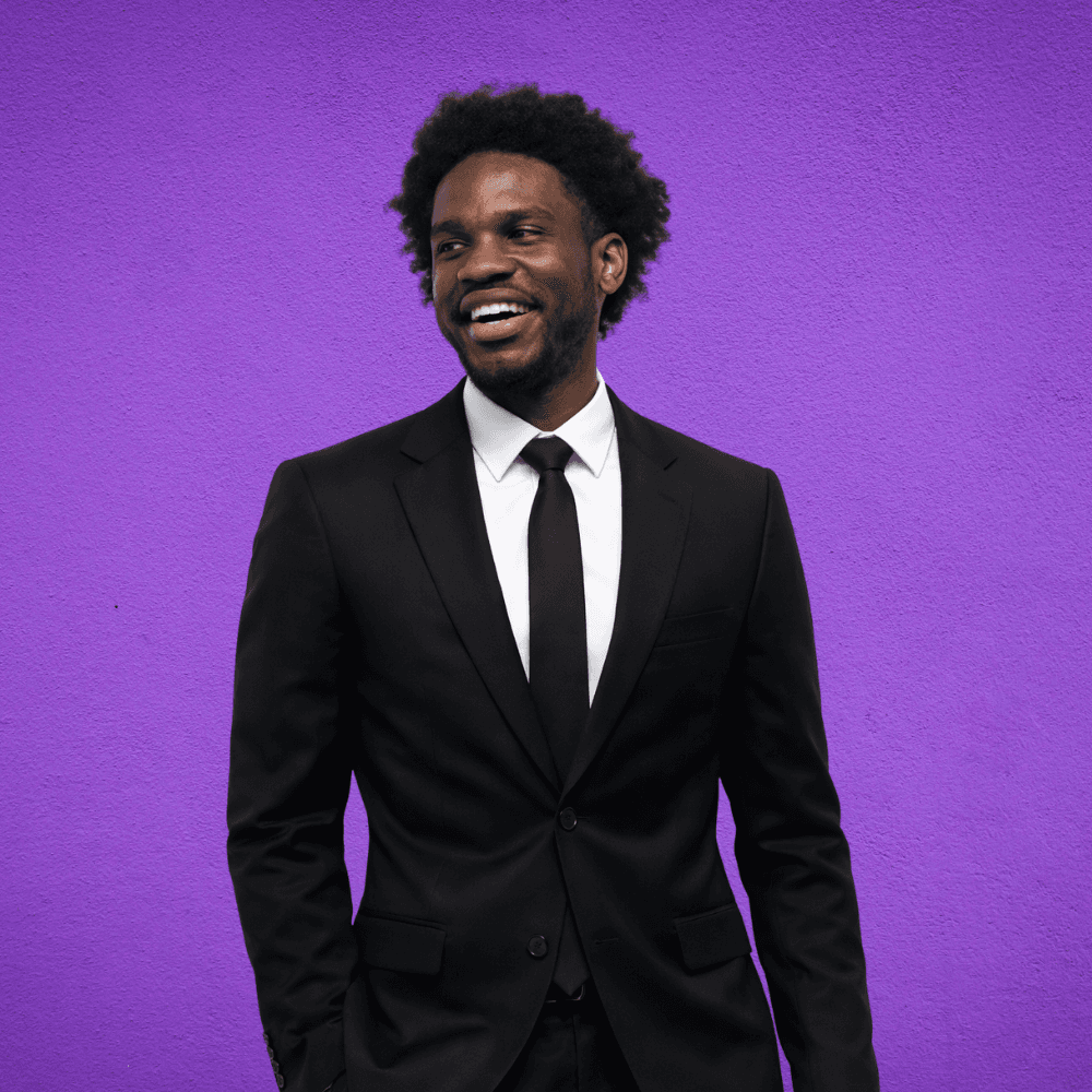 a man in a suit smiling and standing in front of a purple background