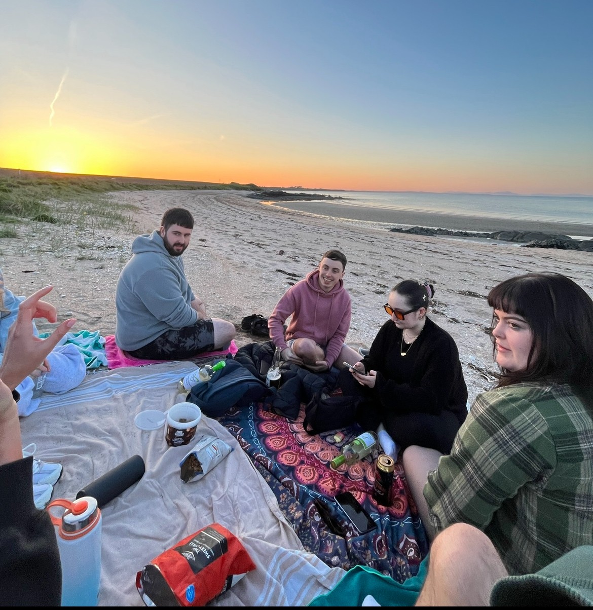 A young woman with long hair smiles while standing against a green backdrop, wearing a casual dark sweater.