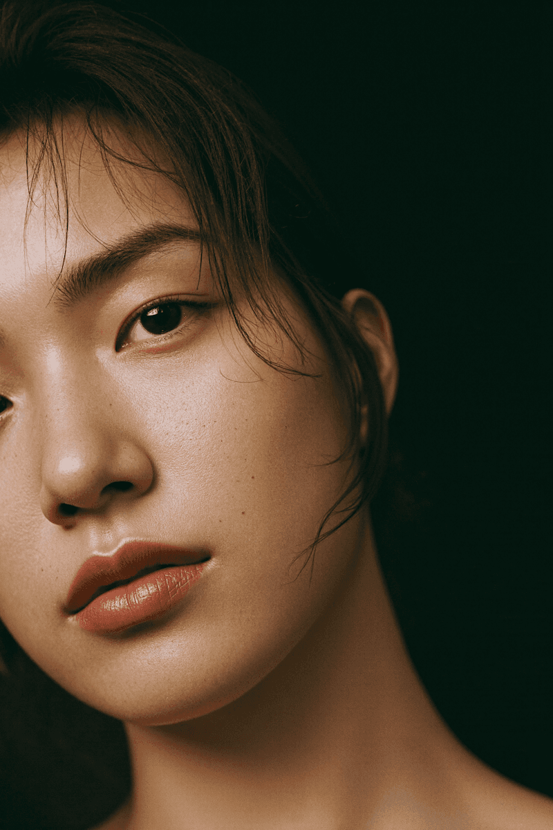 Close-up portrait of a woman with natural skin texture, soft lighting, and a dark background.