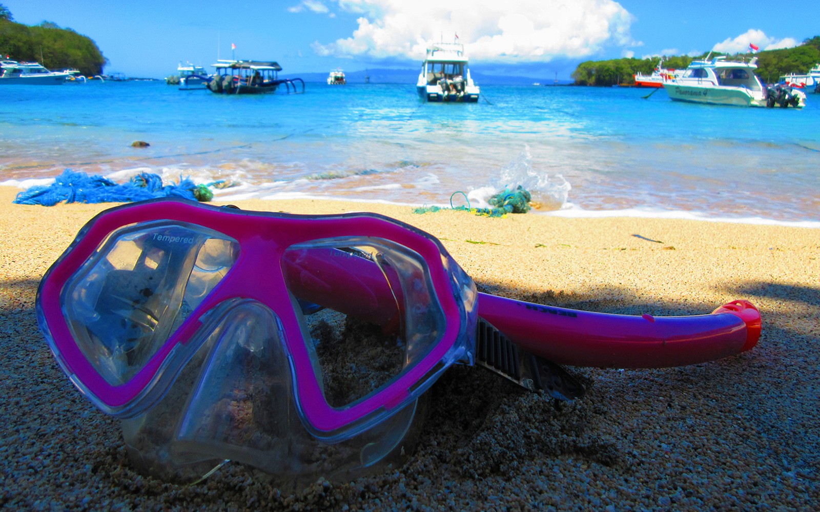 Snorkeling gear on sandy beach with boats in Blue Lagoon, Bali.