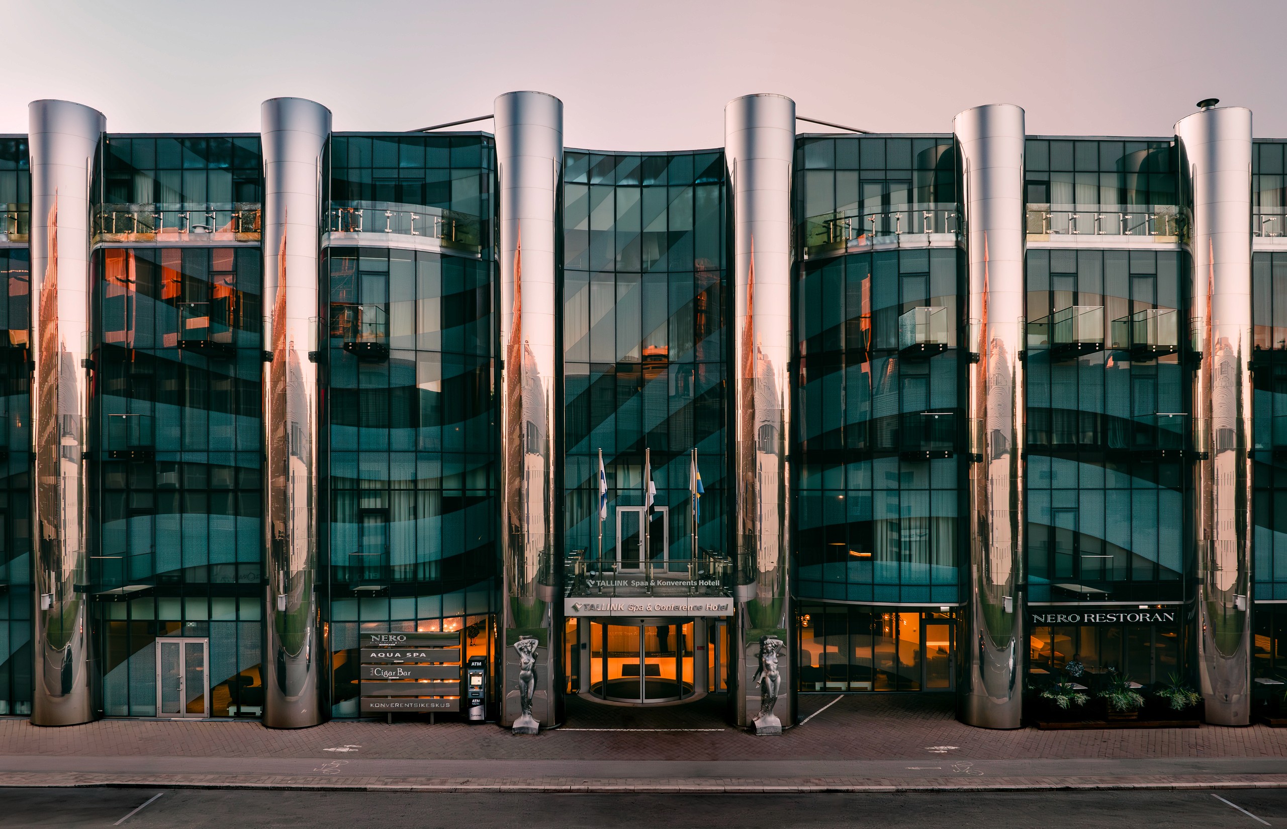 Frontal view of the hotel facade, defined by repeated curved metallic columns and reflective glass bays.