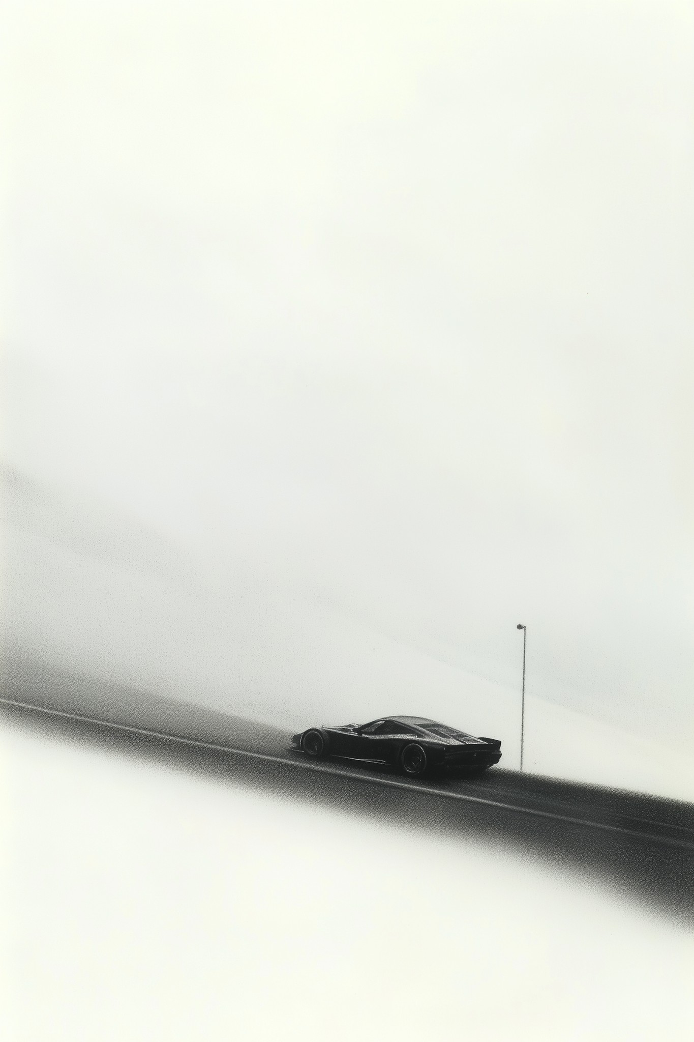 Black sports car driving along an empty road in a foggy, high-contrast monochrome landscape.