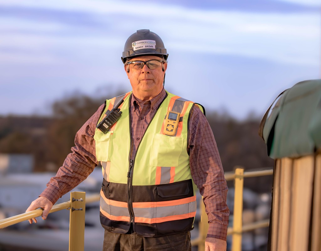 Man in a white shirt focused on a desktop computer displaying charts and data in a softly lit workspace.
