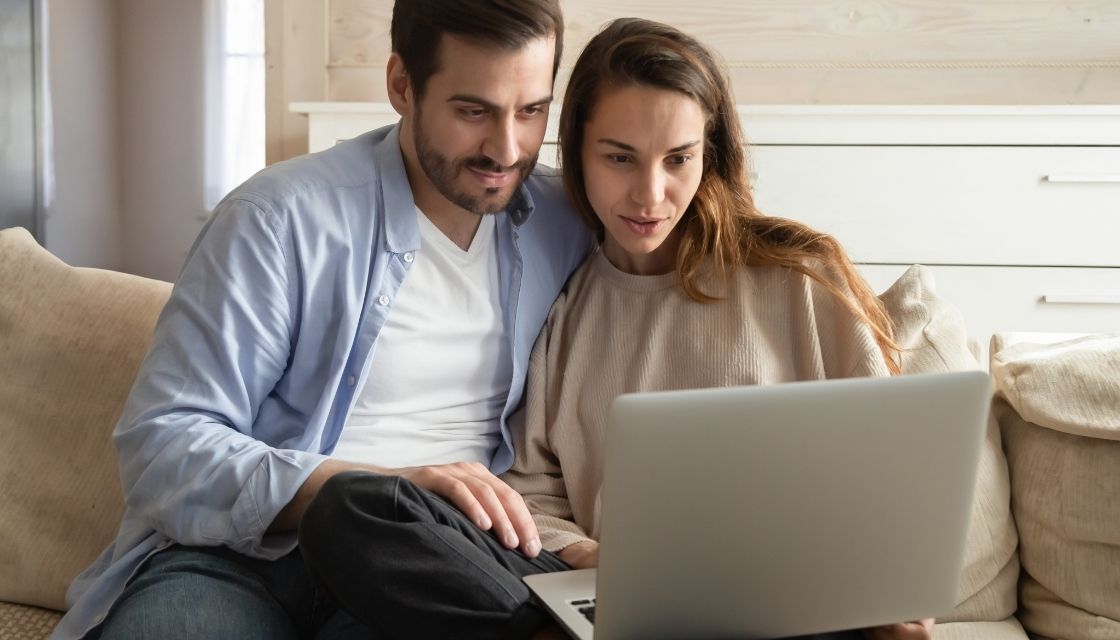 A man and woman sitting closely together looking at a laptop computer