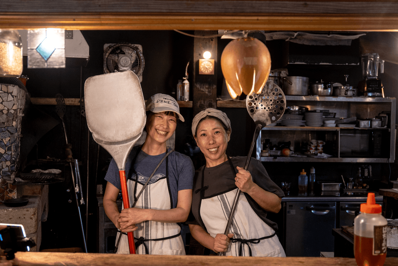 Two team members from Chaya Amamaki posing holding pizza making utensils