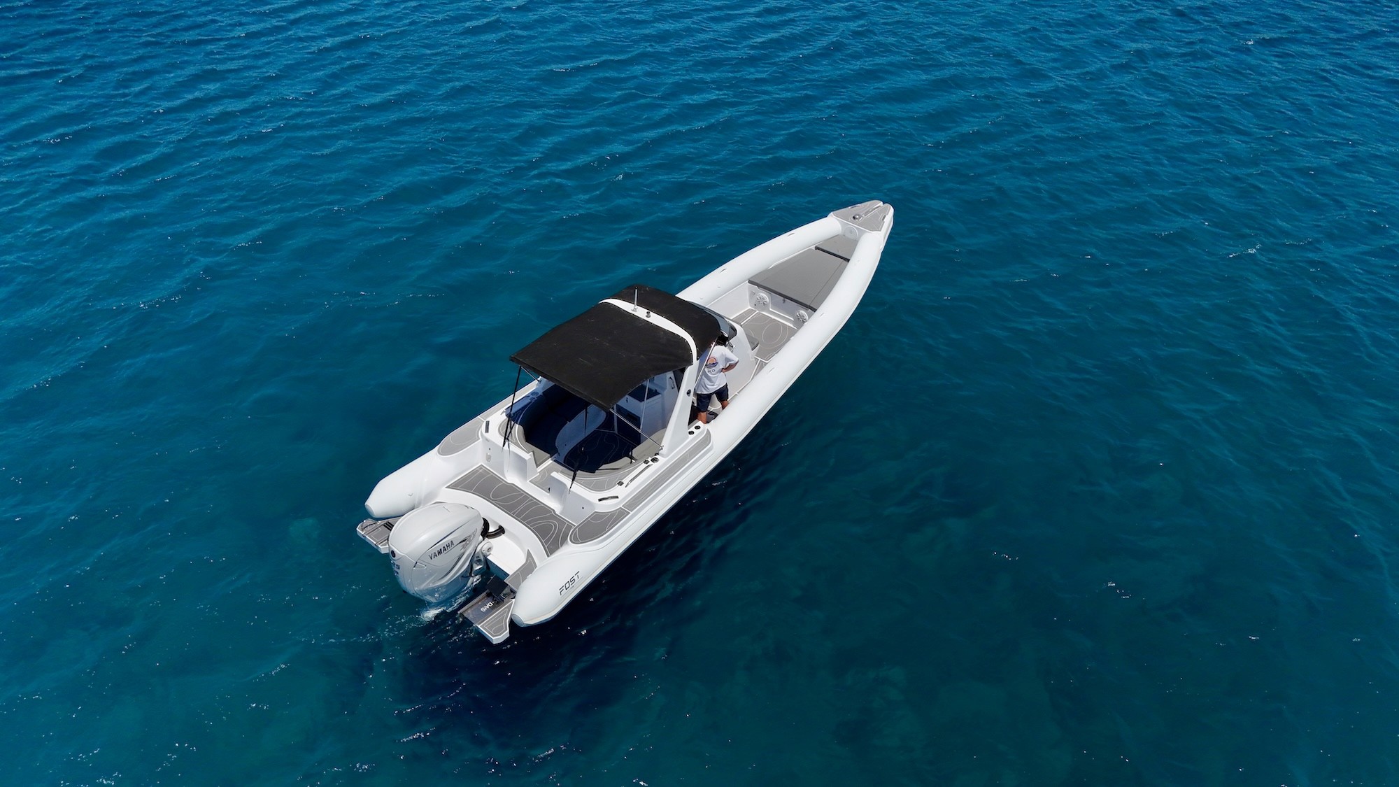 Aerial view of white Fost Matrix 32 speedboat with black hardtop cruising through crystal-clear turquoise waters of the Aegean Sea.