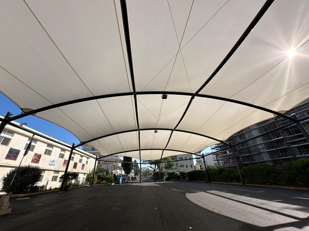 Large beige curved canopy over a paved outdoor area with buildings and trees in the background.