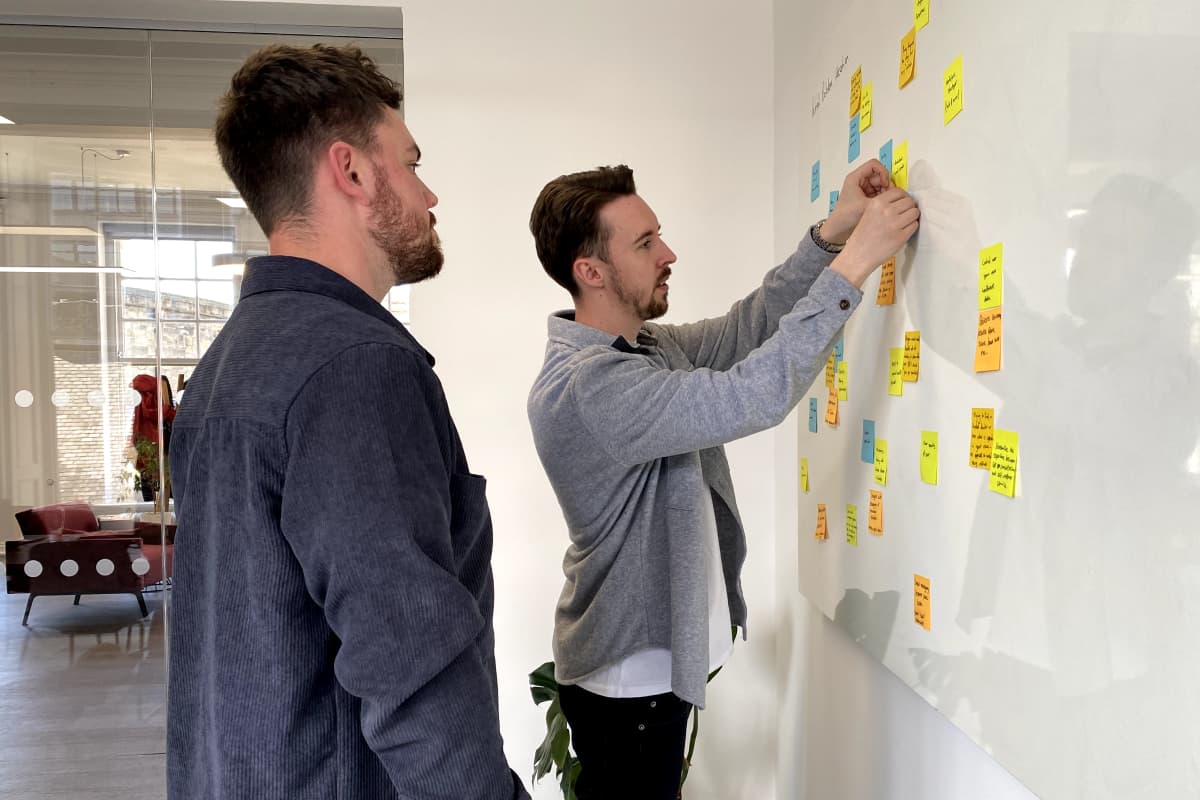Two of the designers arrange post-it notes on a large whiteboard in the Komodo studio