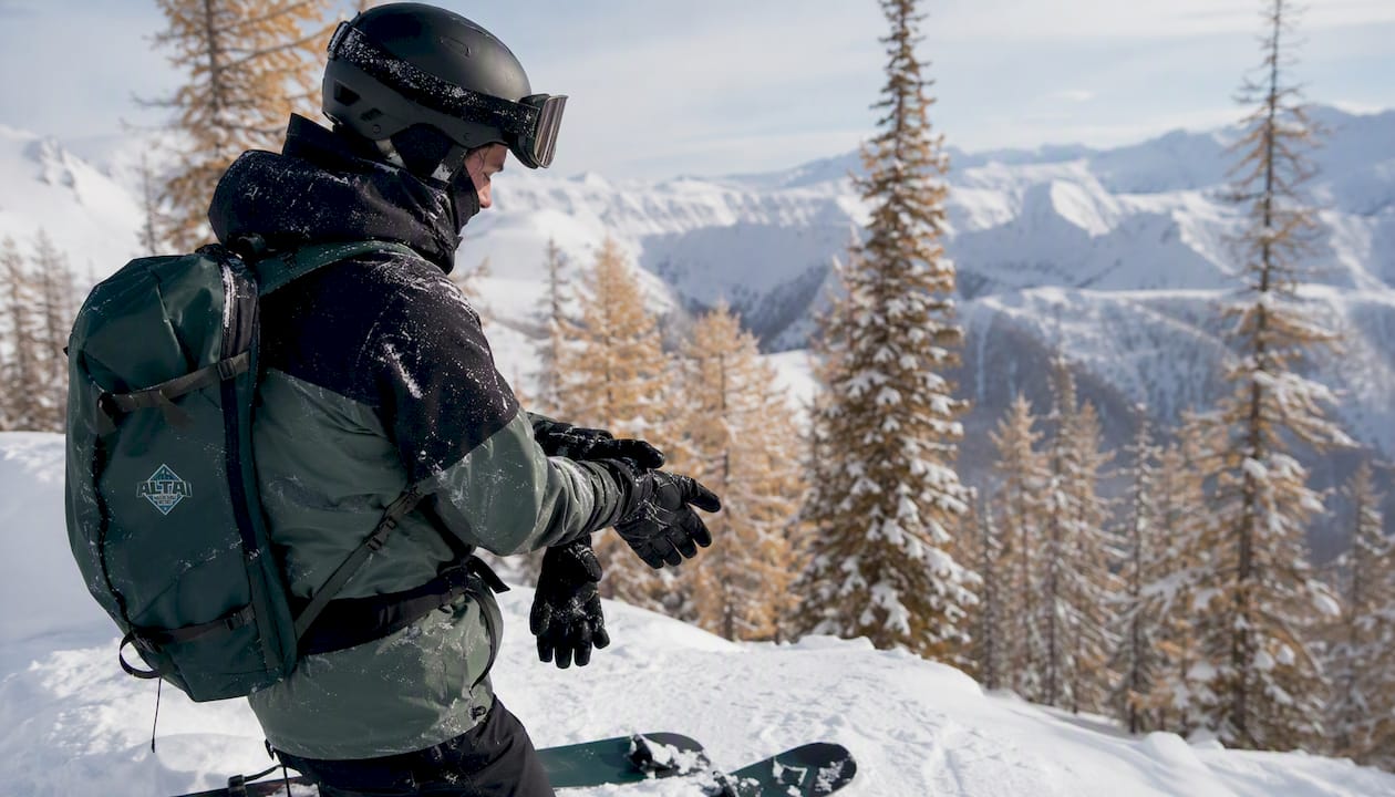 Freeride skier wearing a helmet and adjusting gloves in snowy terrain