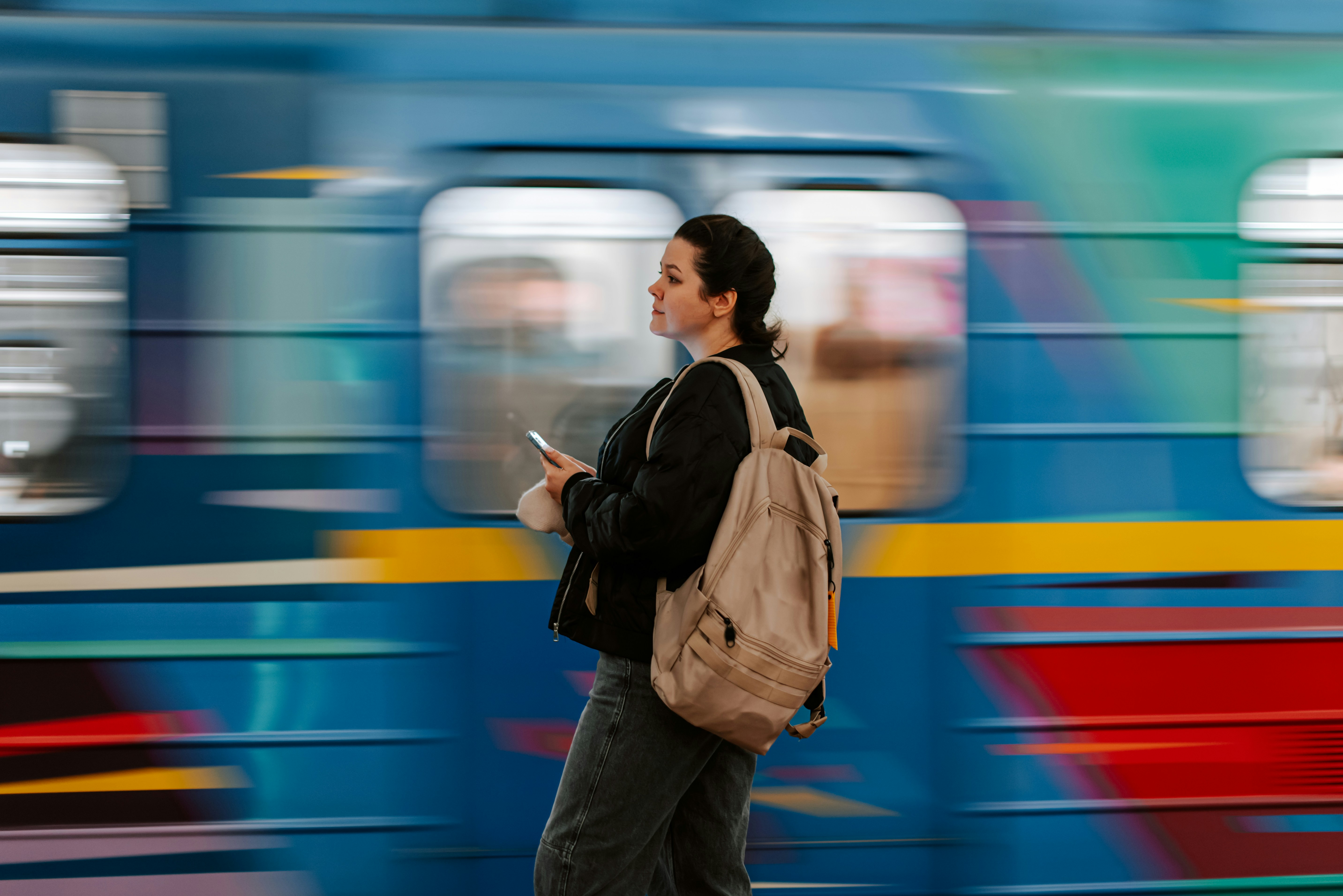 Back view of a woman in a beanie and denim jacket waiting on a train platform in the Netherlands, representing the return journey of Ukrainians from the EU.