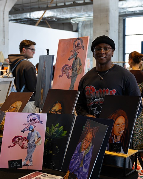 Zdjęcie przedstawiające artystę na stanowisku targowym ze swoimi pracami.