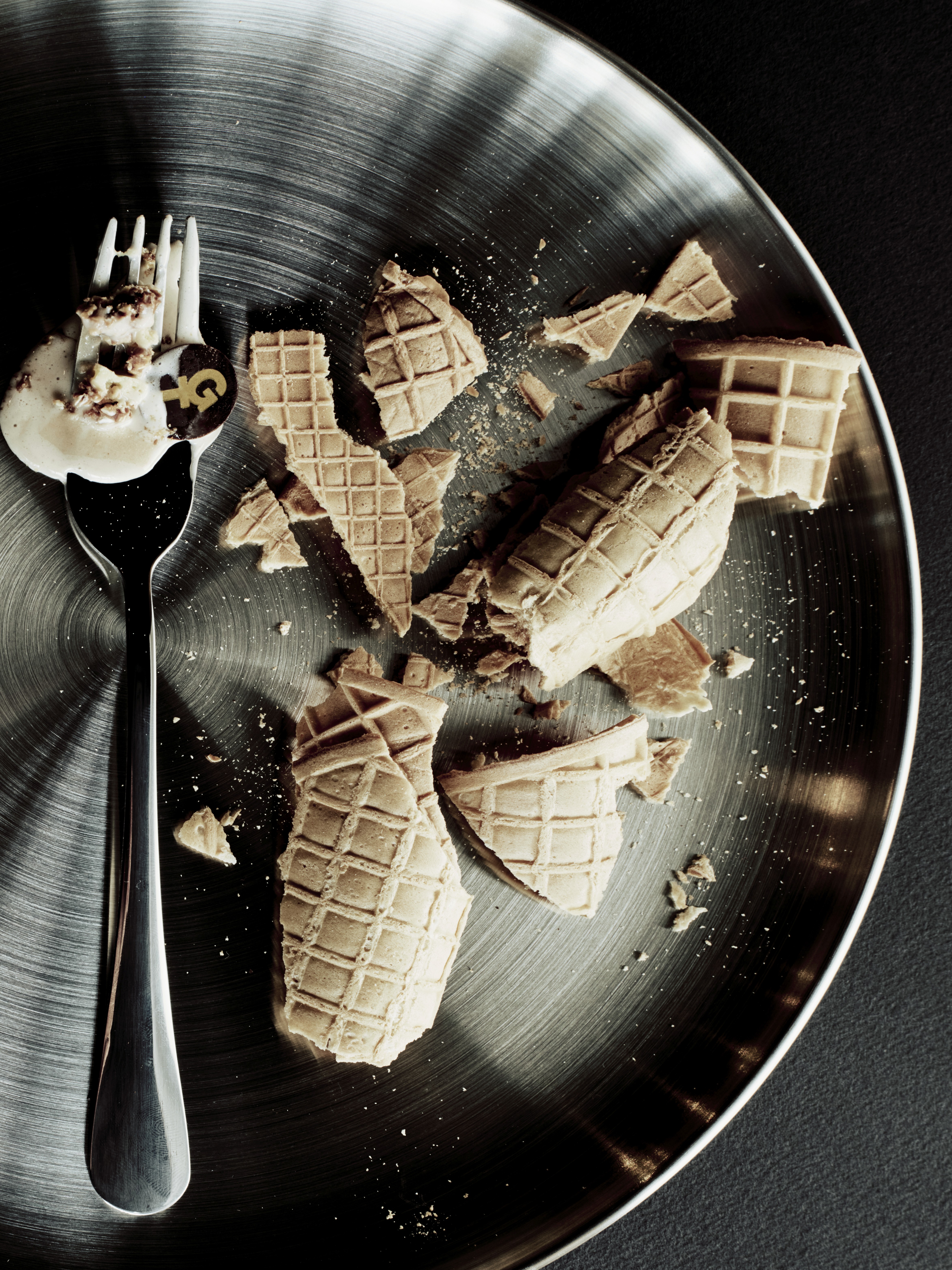 Éclats de gaufrette et reste de dessert sur assiette métallique, avec fourchette portant une bouchée