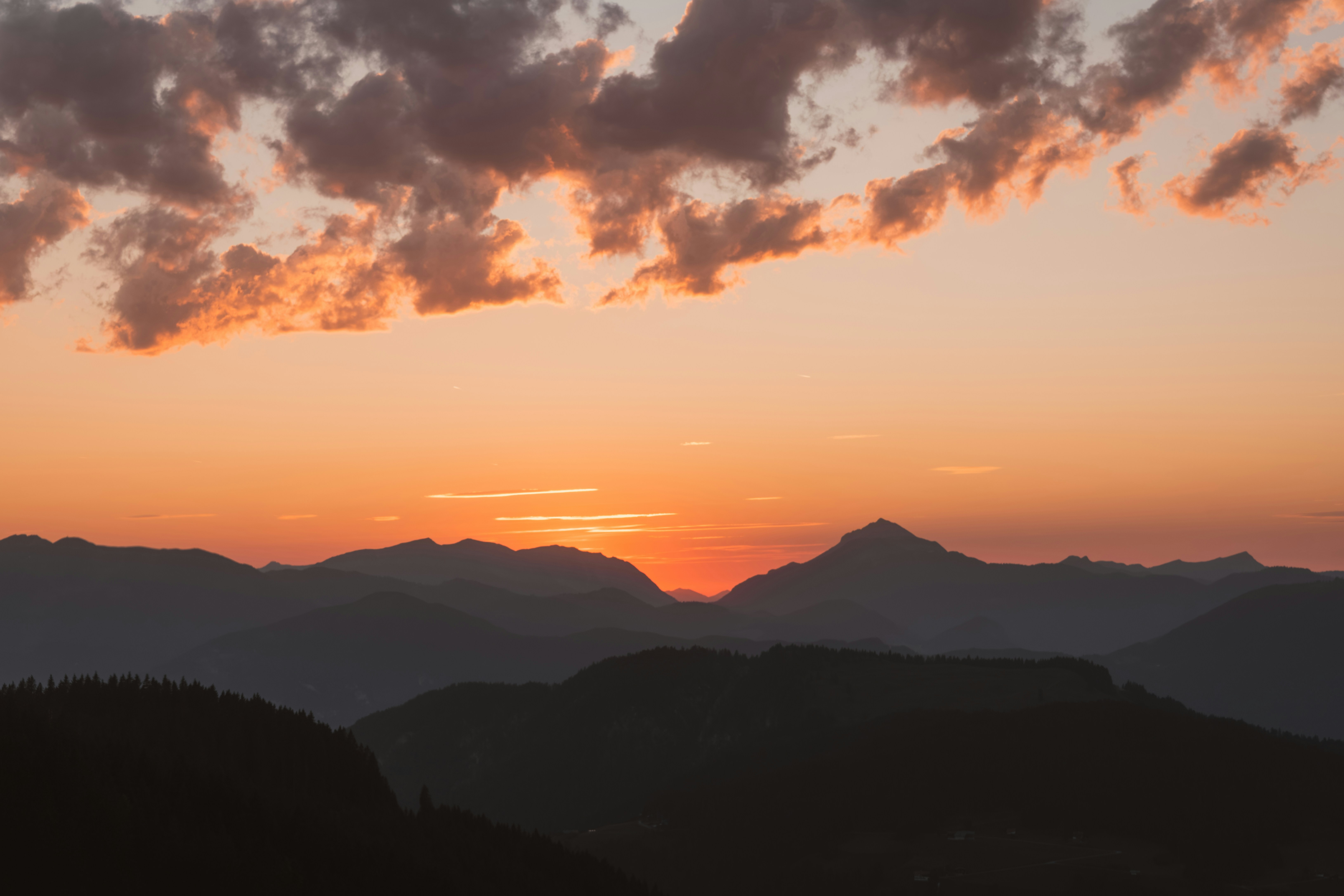 Sunset over silhouetted mountain ranges with orange clouds