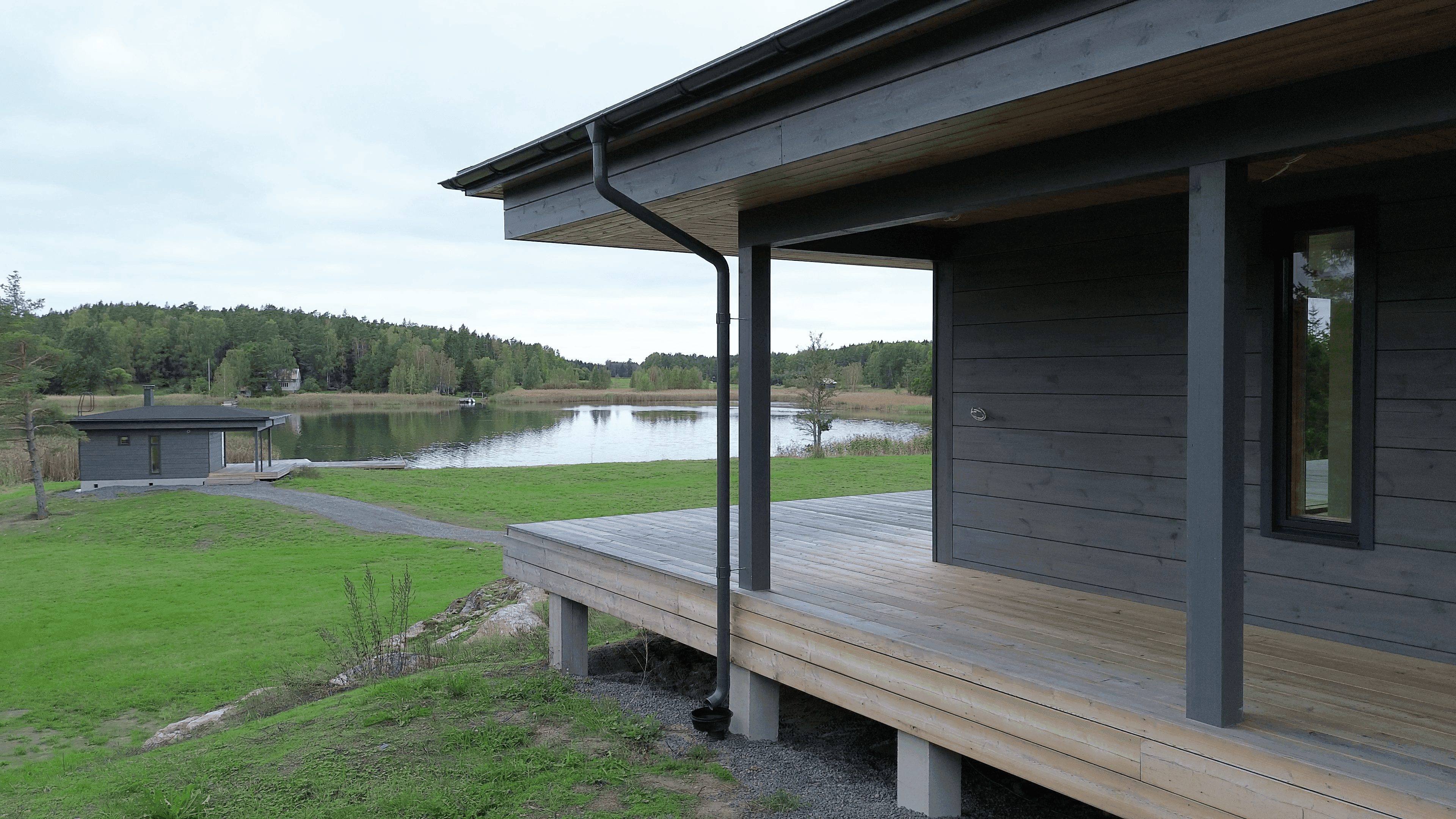 A house shown from the side, with a sauna building and the sea behind it.