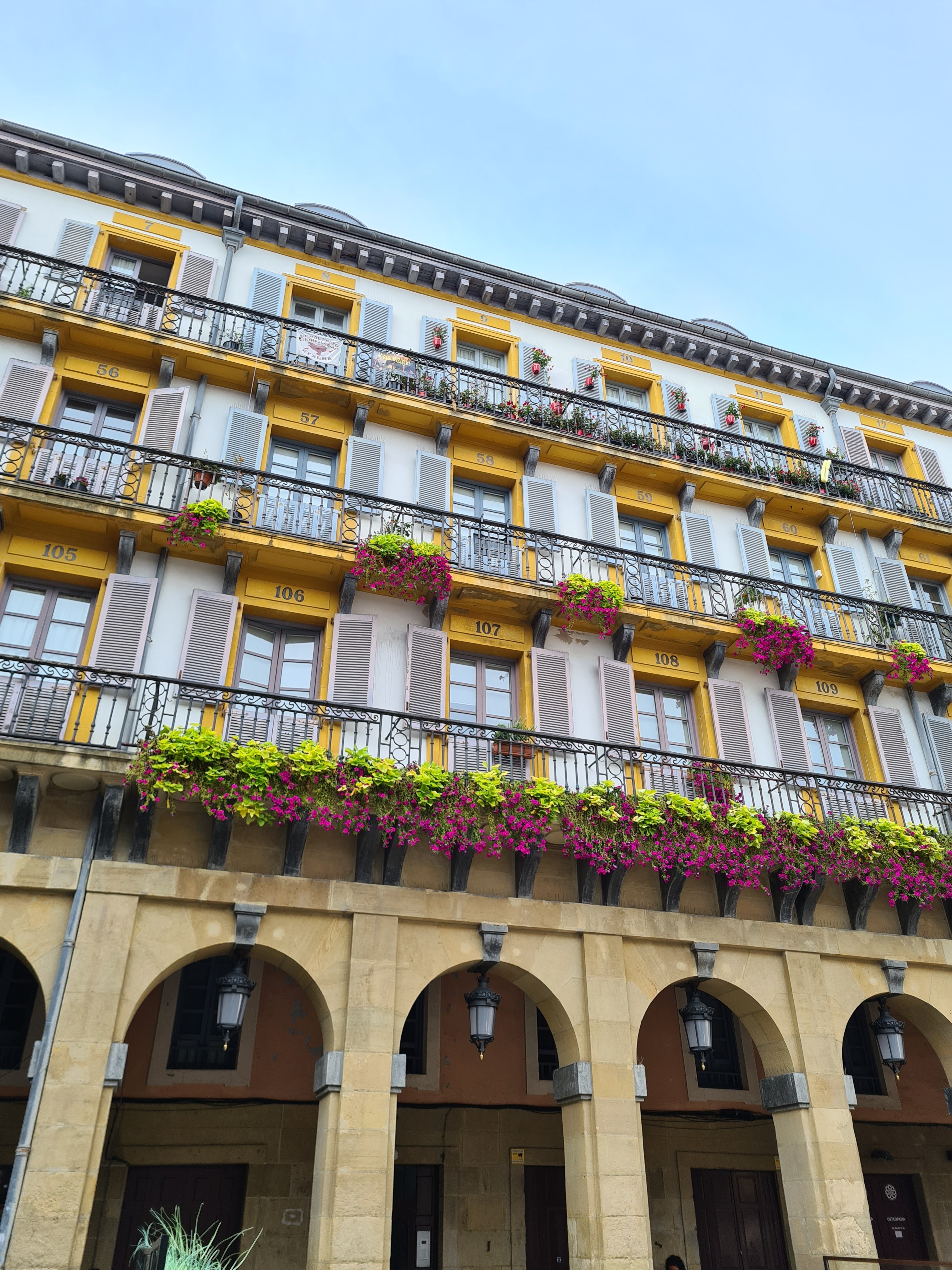 A person walks along a seaside pathway, gesturing with one hand, wearing a jacket and casual shoes.