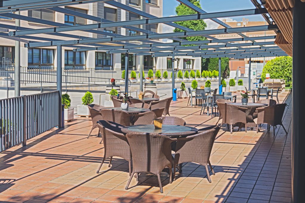 Outdoor terrace with wicker seating under a metal pergola structure.