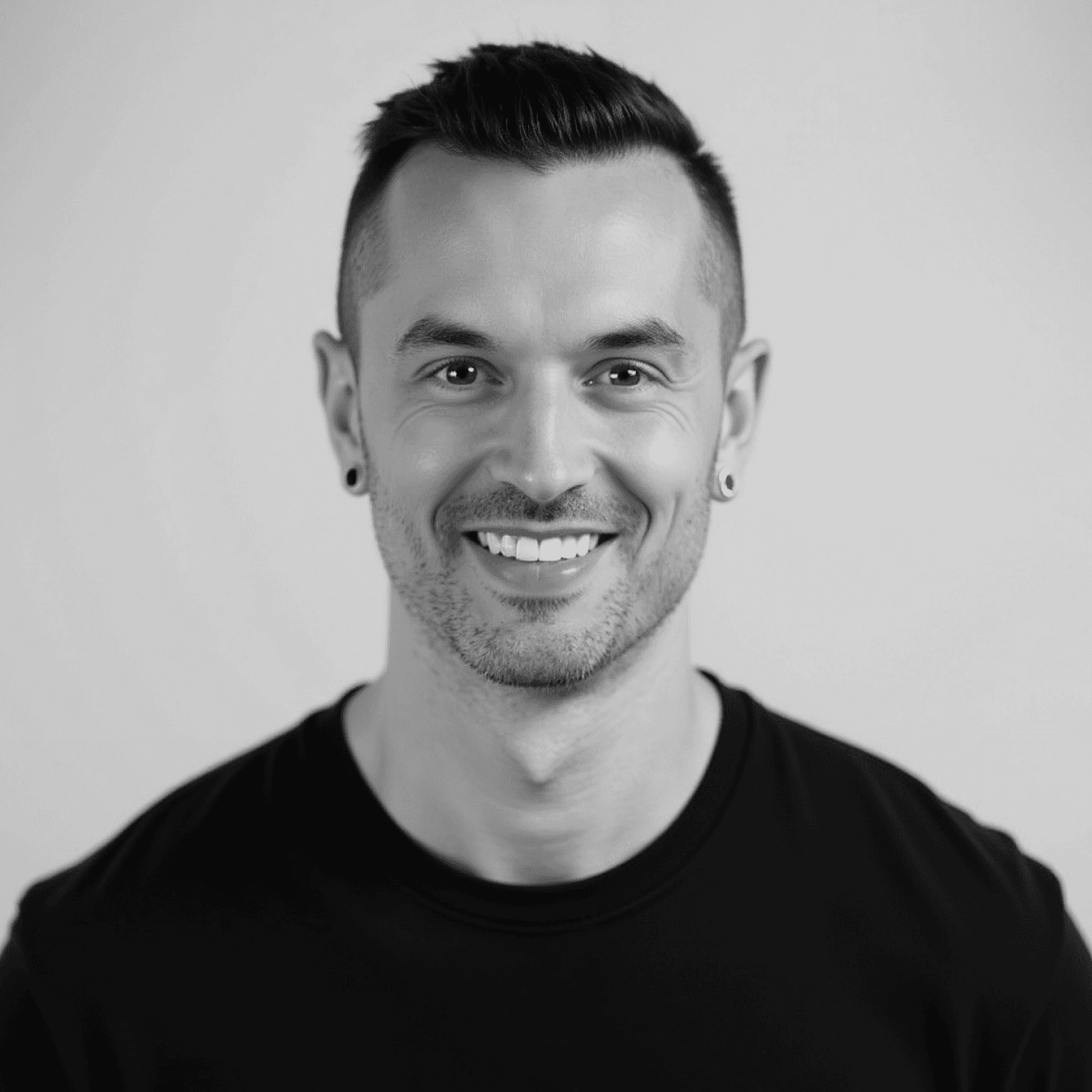Portrait of a young man with short hair, wearing a dark t-shirt, against a plain background.