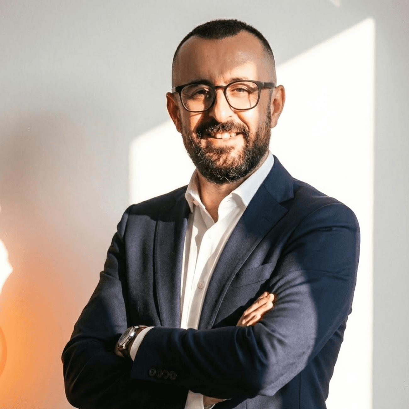 A man with glasses and a brown shirt, crossing his arms.