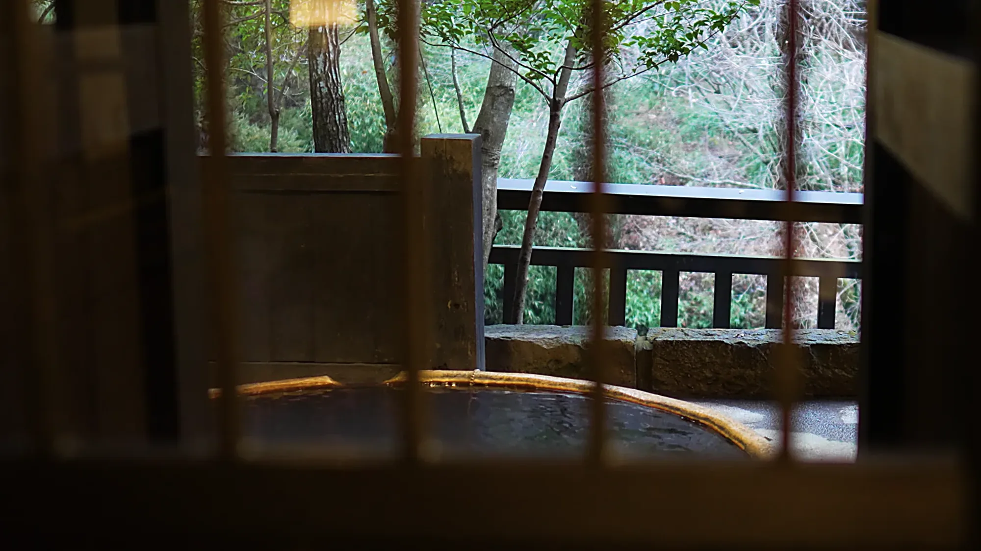 A round timber tub at Kurokawa Onsen seen through a window frame, forest beyond
