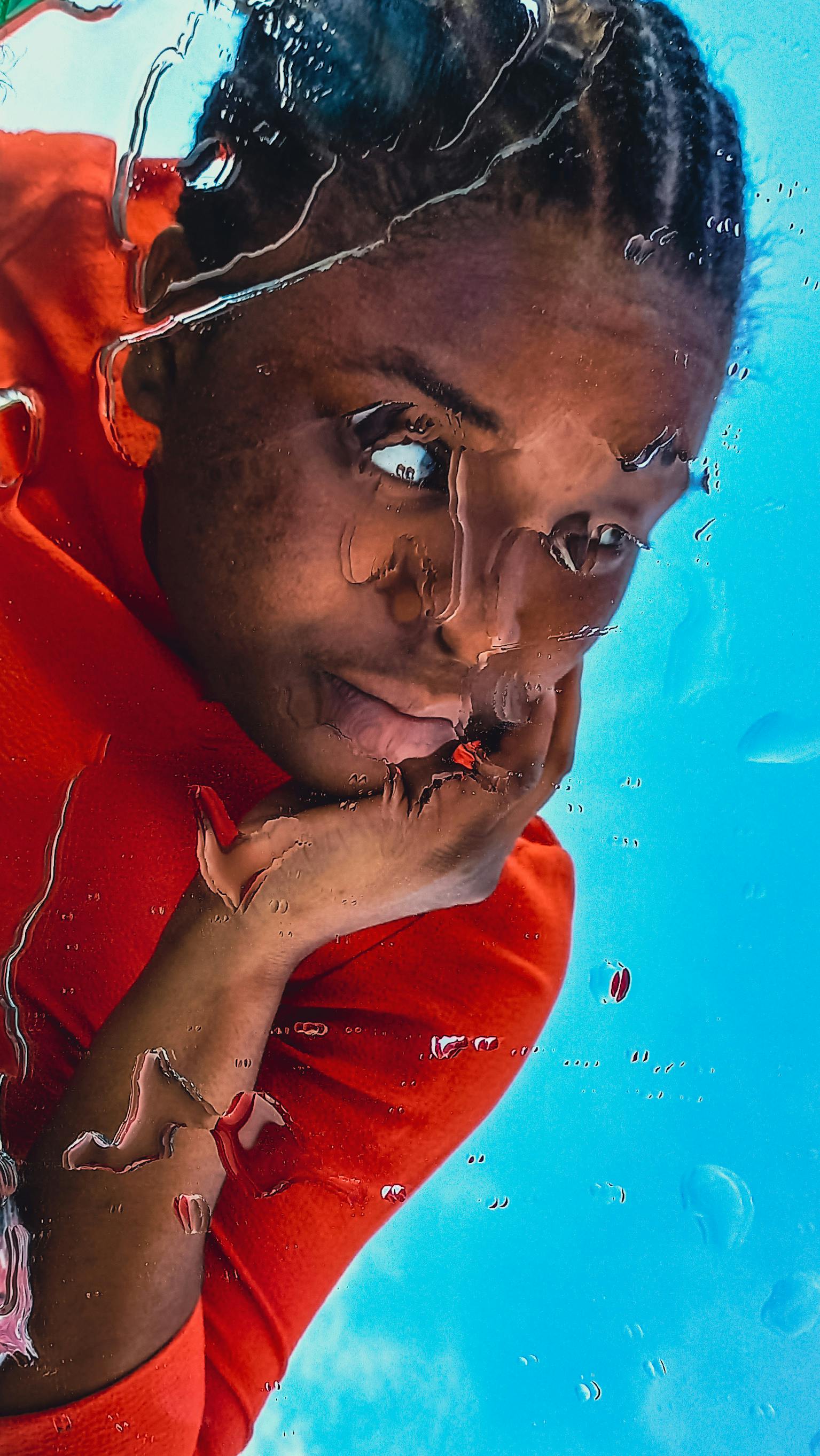 Close-up portrait of a person behind rippling glass against a bright blue background