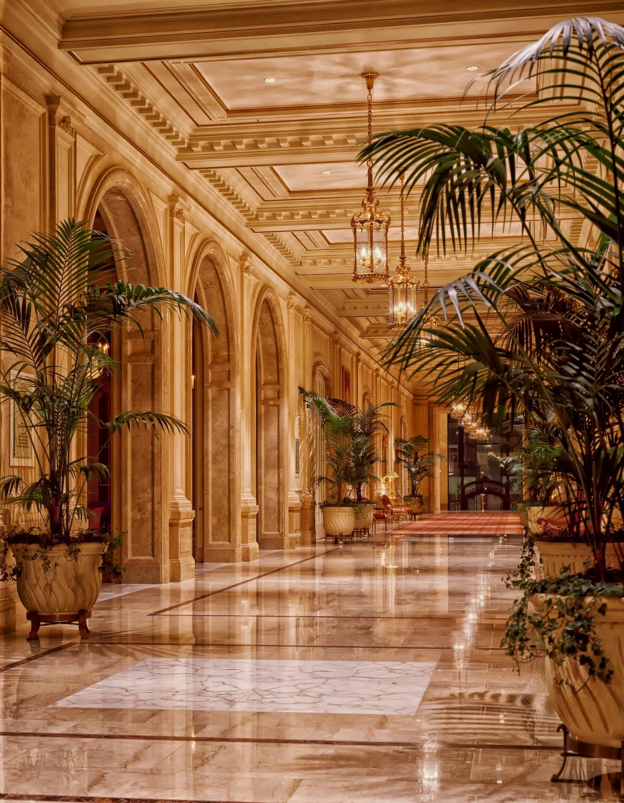 Outdoor corridor with brick arch windows, stucco grid wall, wooden pergola, and dramatic sunlight shadows.