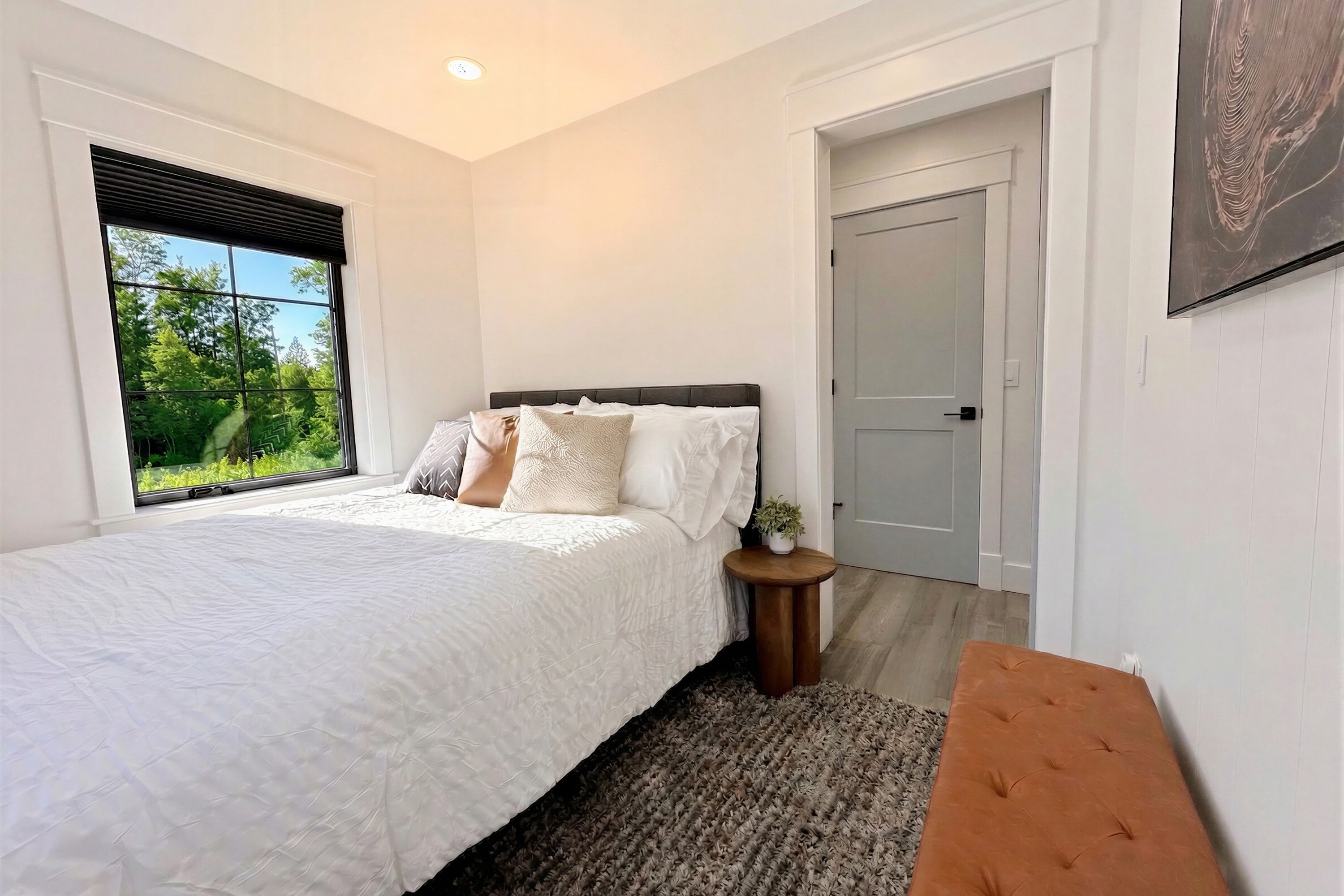 Guest bedroom with white linens and a window facing the trees