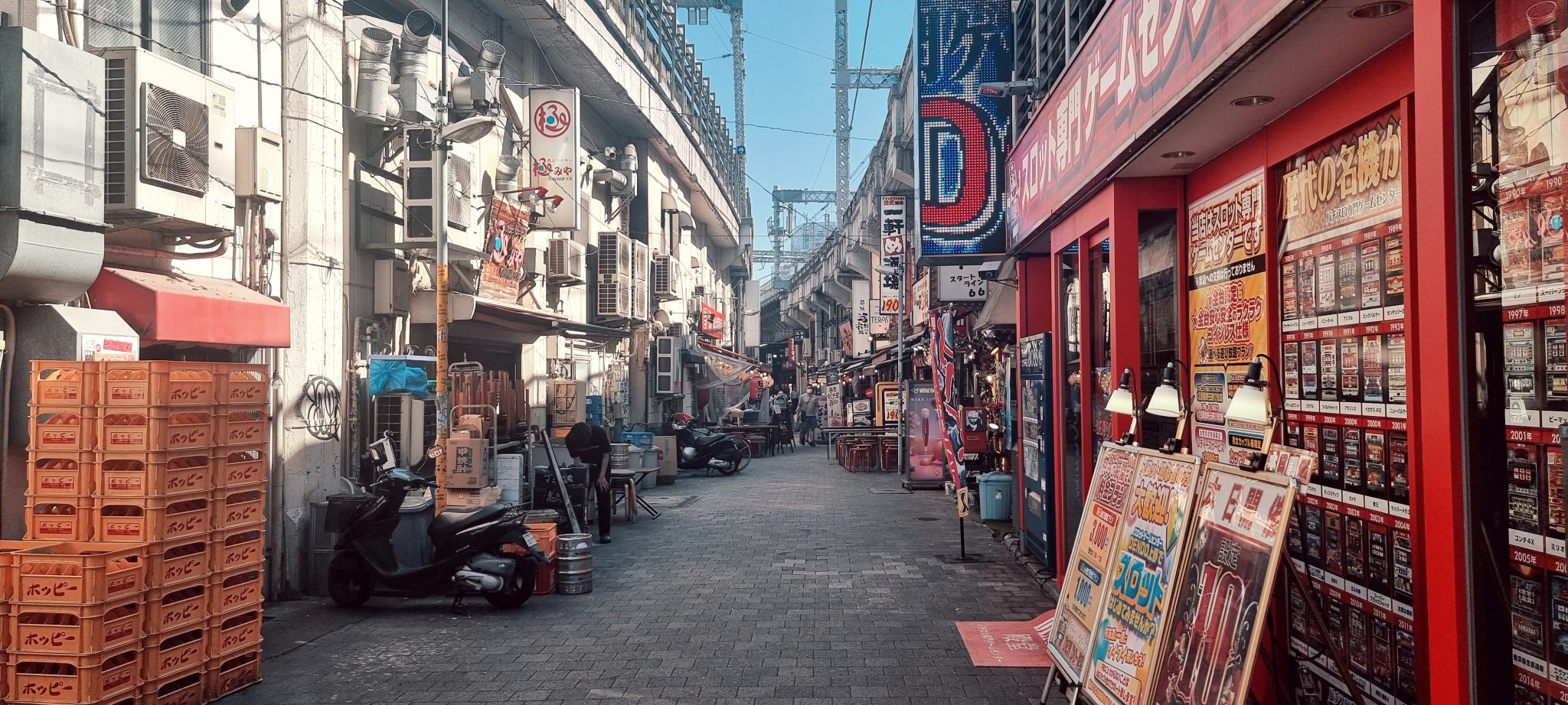 Narrow Japanese alleyway lined with drink crates, scooters and illuminated shop signage