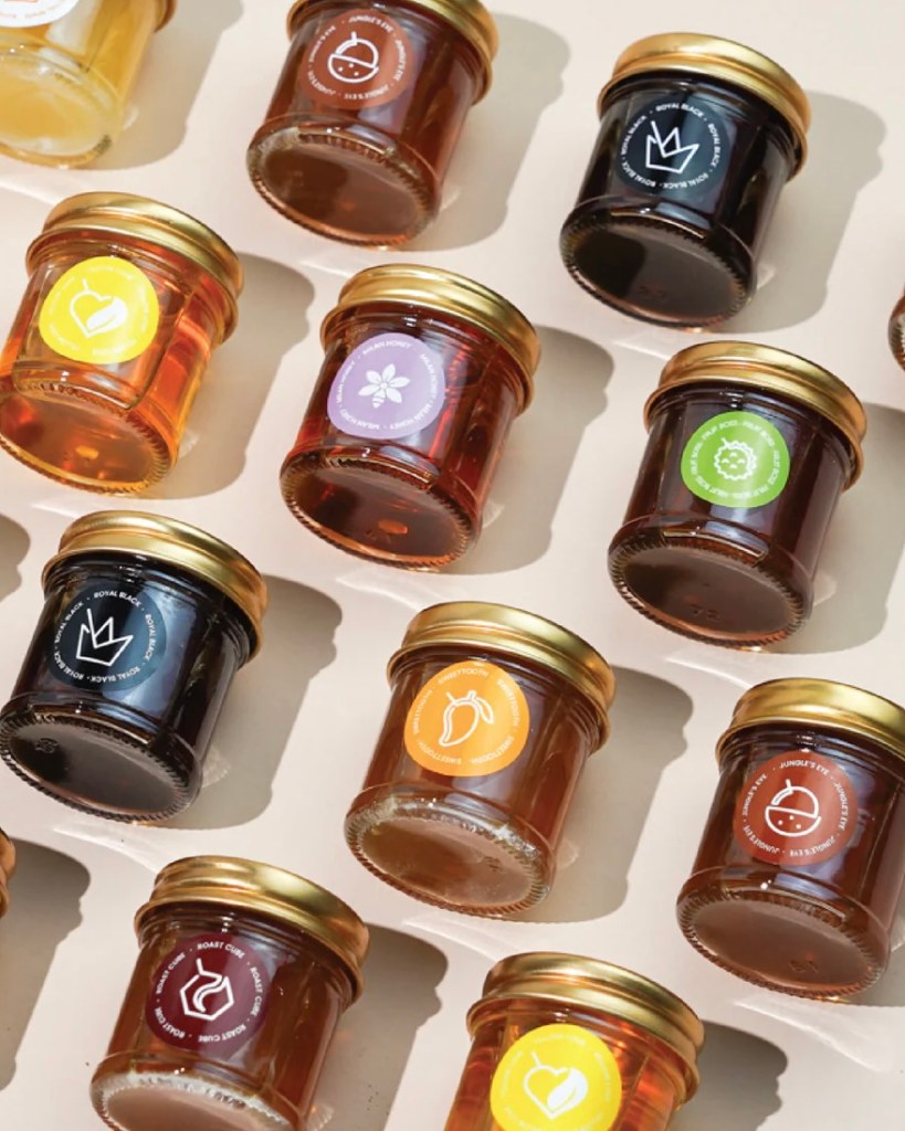 Assorted jars of honey with different colored labels arranged on a light background.