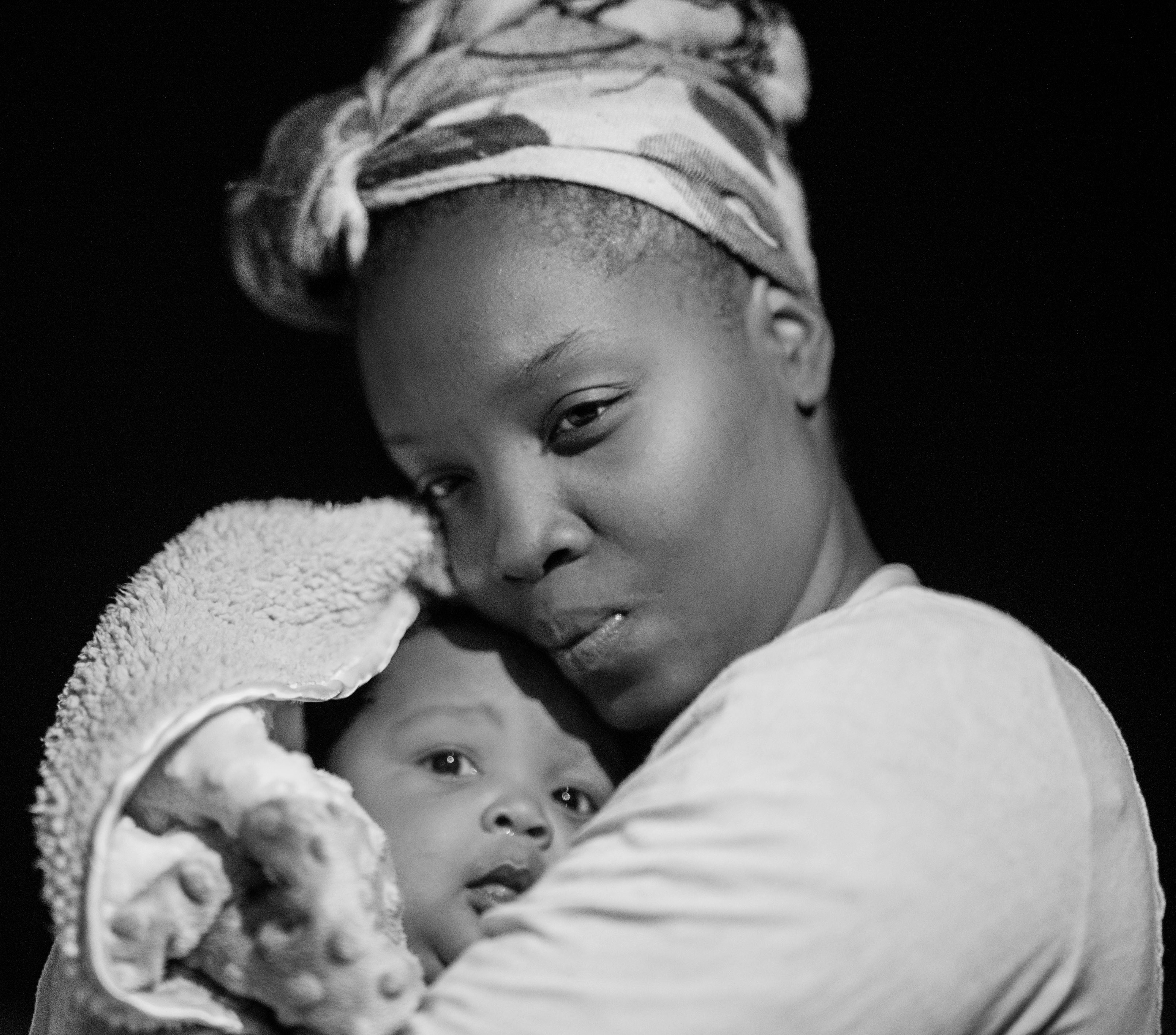 Black-and-white portrait of a mother in a headwrap holding her baby close to her face.