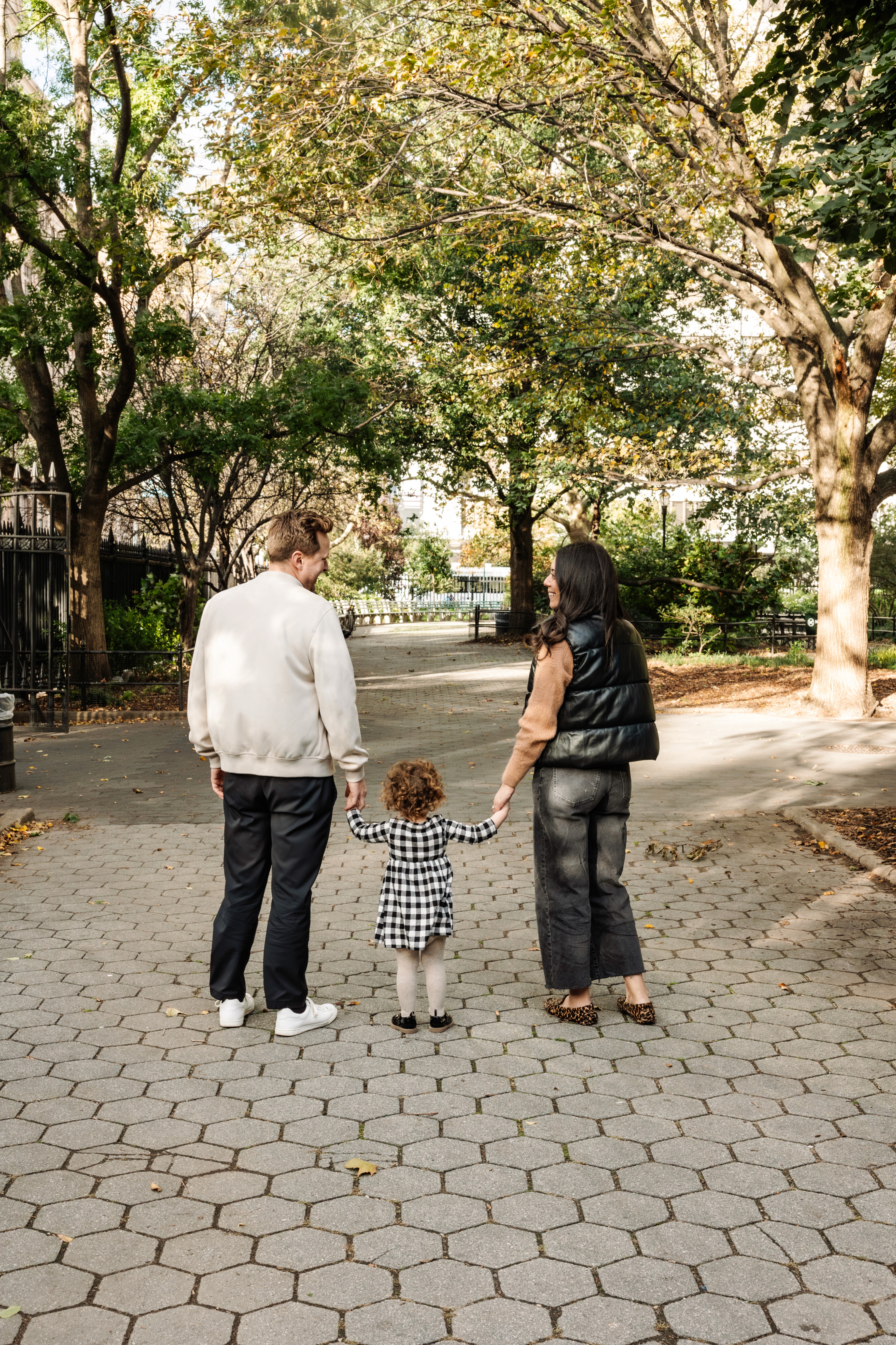 Mom holding her daughter close while dad stands proudly by their side at Stuyvesant Square Park in the Gramercy and East Village neighborhood of NYC — warm, candid family photography by Lizz Spano Photography, New York City family photographer.