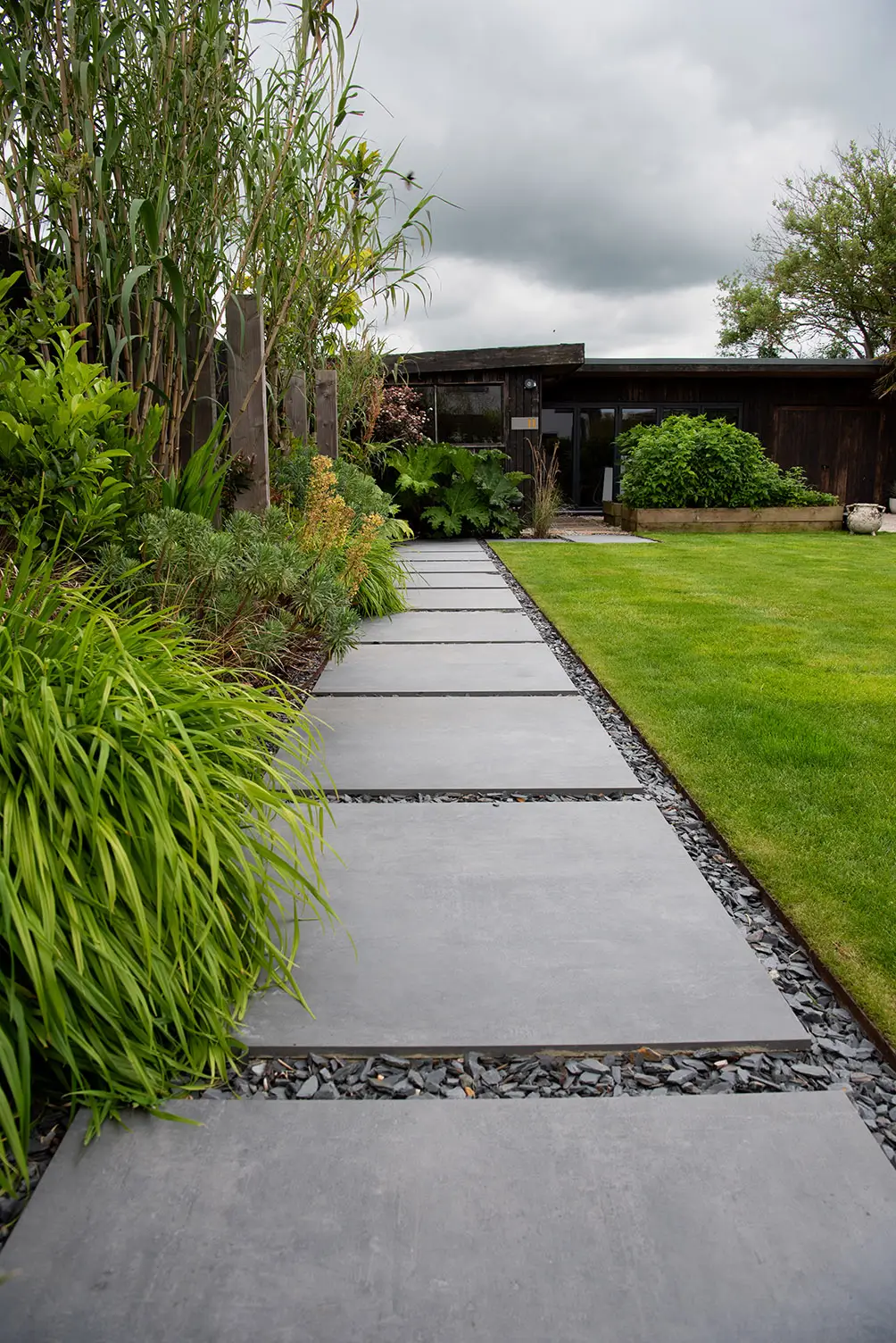 A stone pathway leads through a lush green garden, with cloudy skies in the background.