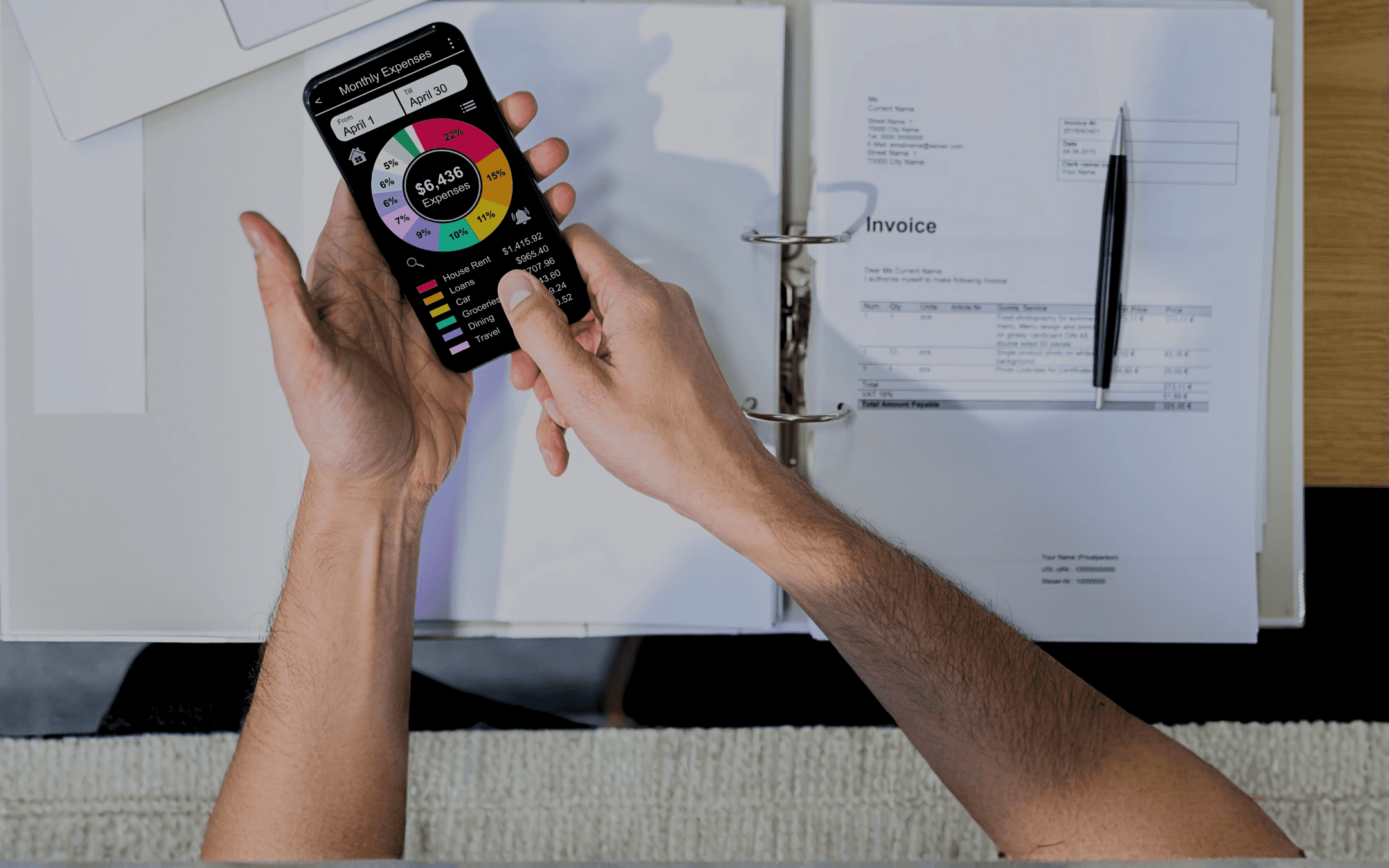 Person holding phone displaying a pie chart of a business plan with documents, and pen in a binder.