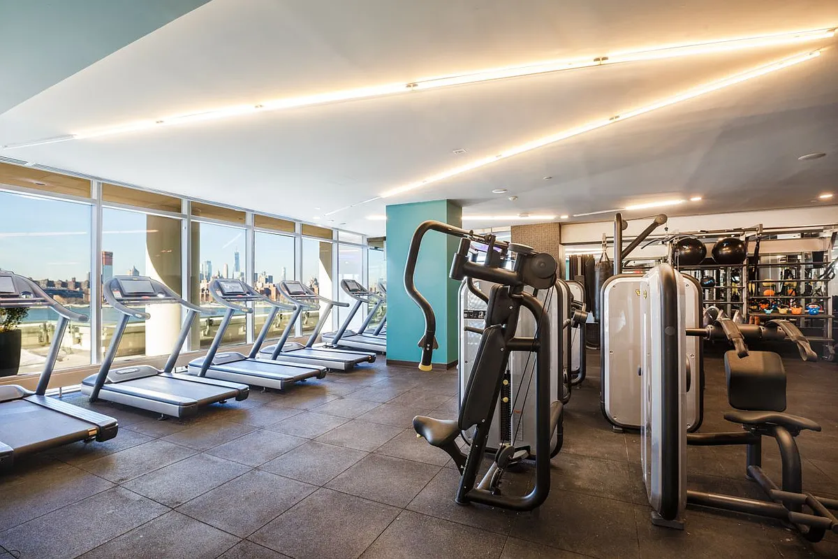 Interior of a gym with treadmills and expansive windows showcasing the cityscape outside.