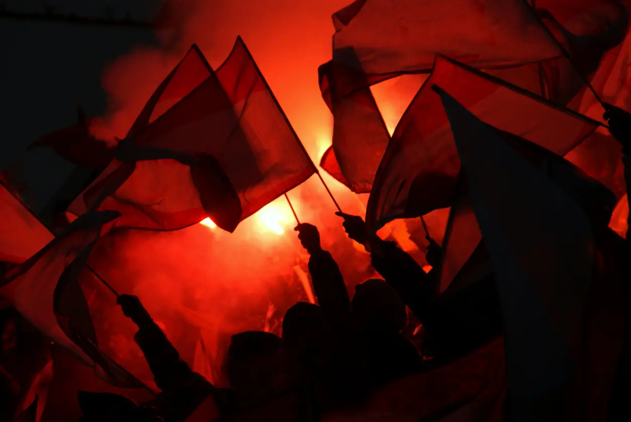 Silhouettes of protesters waving flags lit by red flares at night, illustrating the in-group dynamics that fuel radicalisation