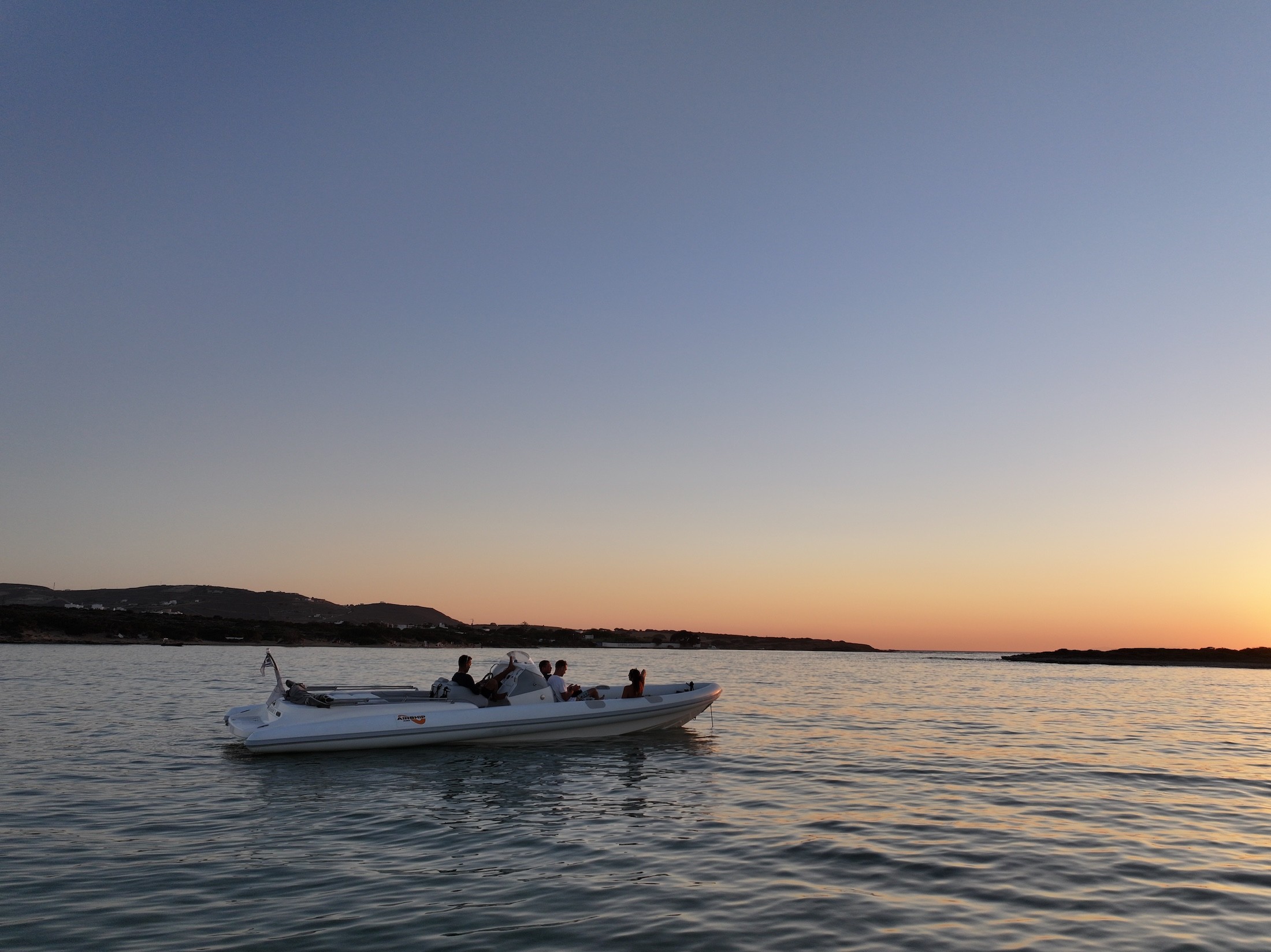 White speedboat with passengers cruising calm waters during golden hour sunset in the Cyclades.