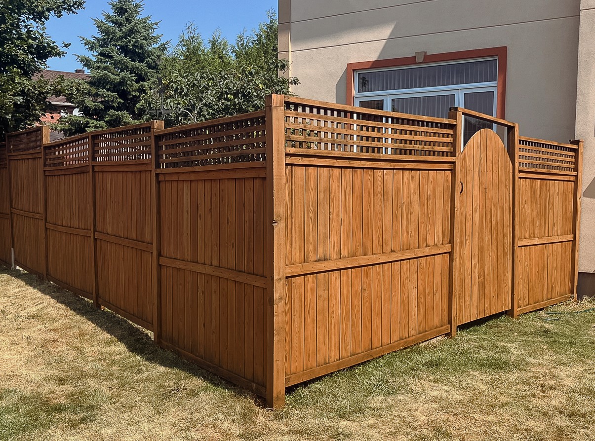 Freshly stained wooden privacy fence along a landscaped backyard.