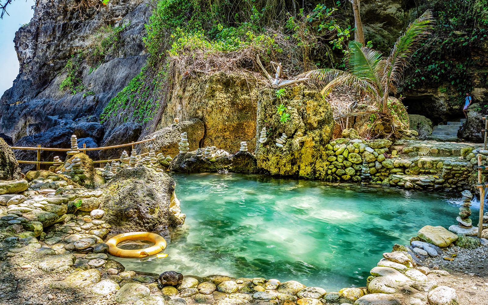 在巴厘岛的坦贝林海滩，欣赏碧绿色水域和石灰岩地貌构成的洞穴泳池风景。