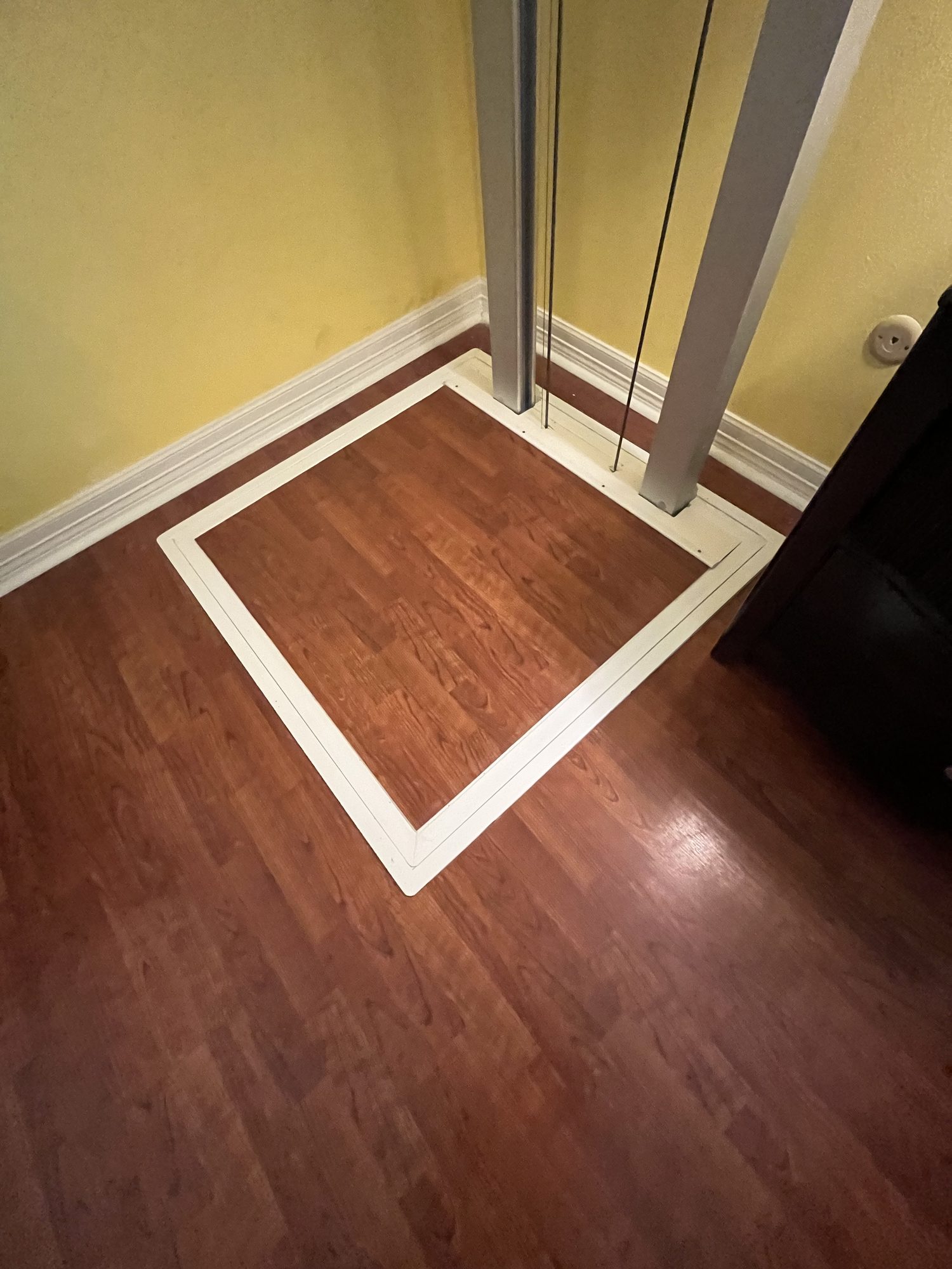 Closed trapdoor sitting flush in the floor with the elevator rails passing through