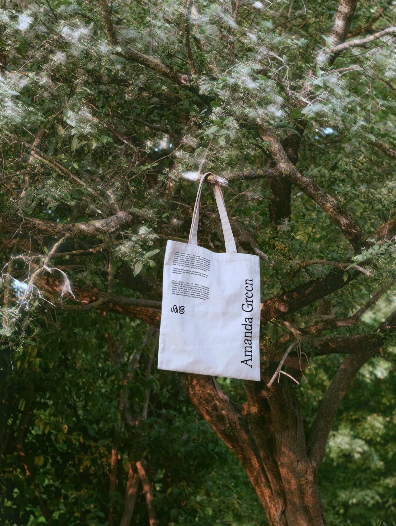 White cotton tote with logo and text, hanging in tree