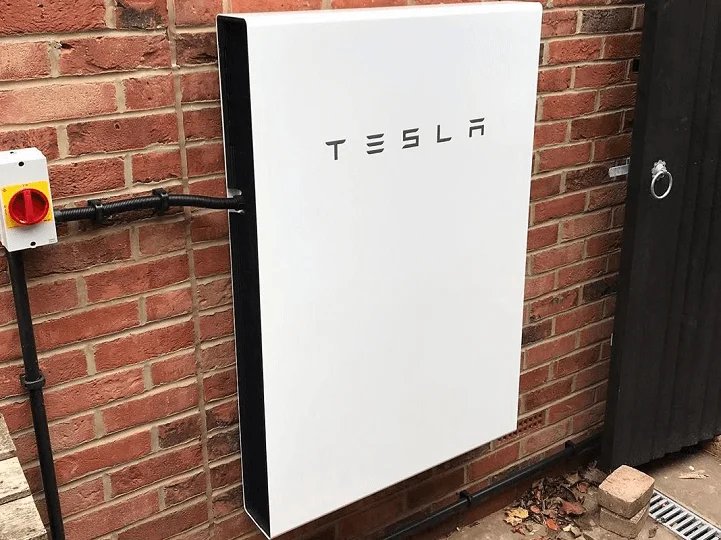 Home battery installed beside an outdoor wall for storing electricity alongside a heat-pump system