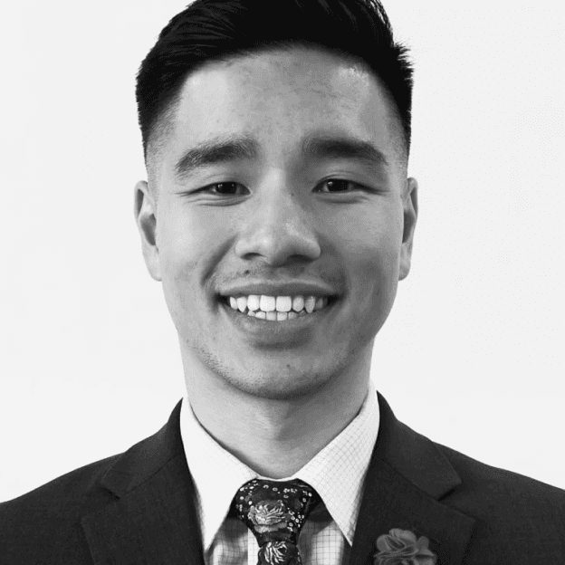 A man wearing a suit and tie, facing forward, smiling. Formal business attire. Confident look.