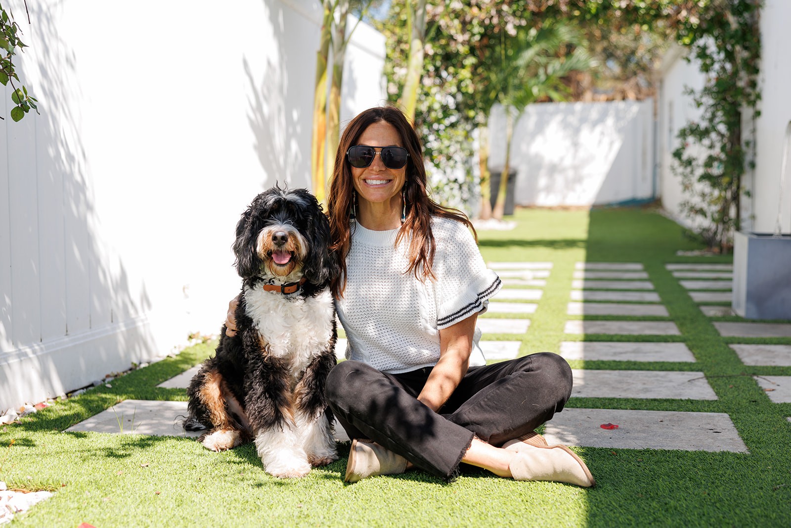 Woman and Bernedoodle dog sitting on artificial grass.