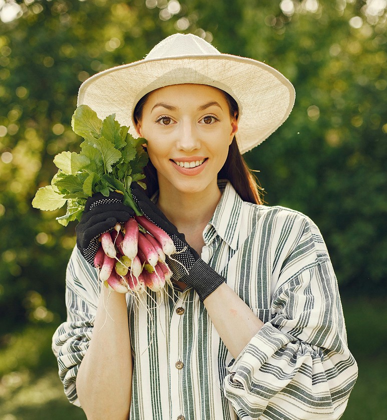 Portrait of Sophia Nguyen, a woman wearing a sun hat holding a bundle of freshly harvested radishes.